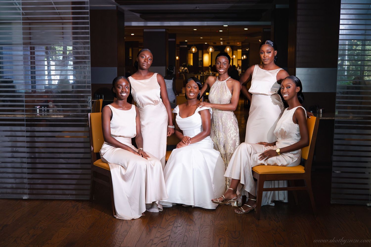 Elegant bridal party poses in cream-colored dresses against modern interior setting.