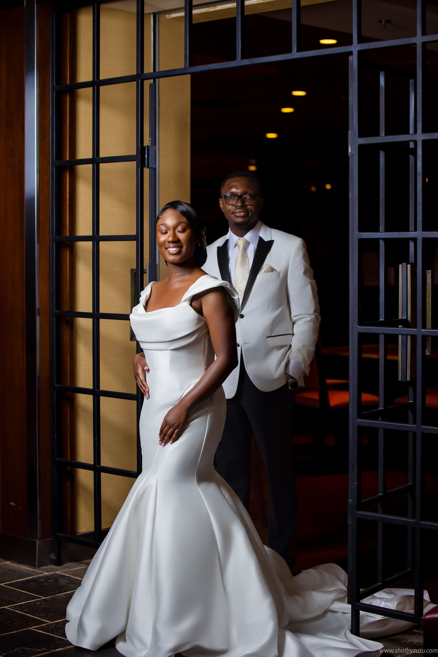 An elegant wedding portrait featuring a mermaid dress and white tuxedo jacket in a modern venue setting.