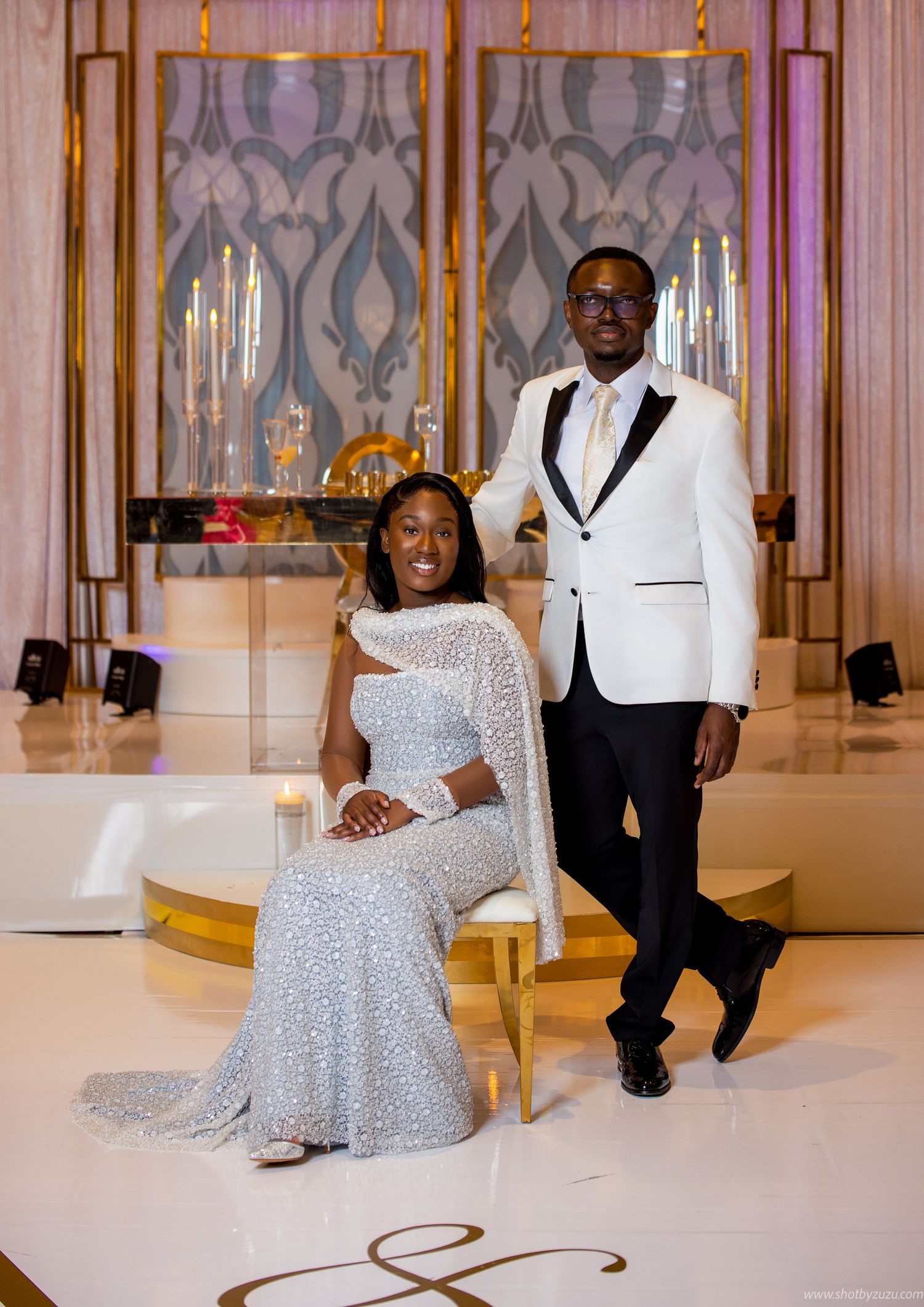 Formal wedding portrait in an elegant venue with candles and decorative patterns in the background.