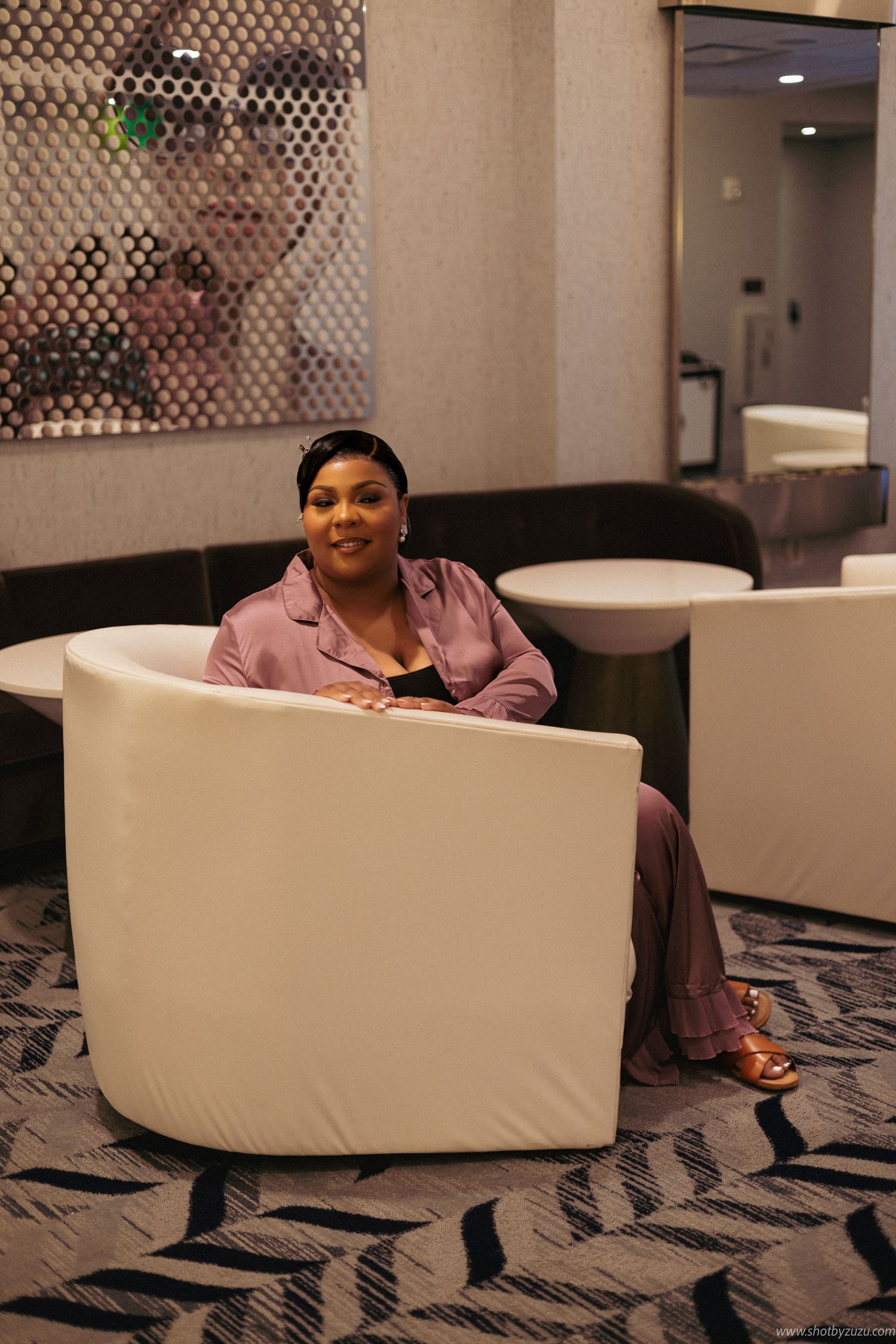 Woman in rose colored loungewear relaxes in white accent chair.