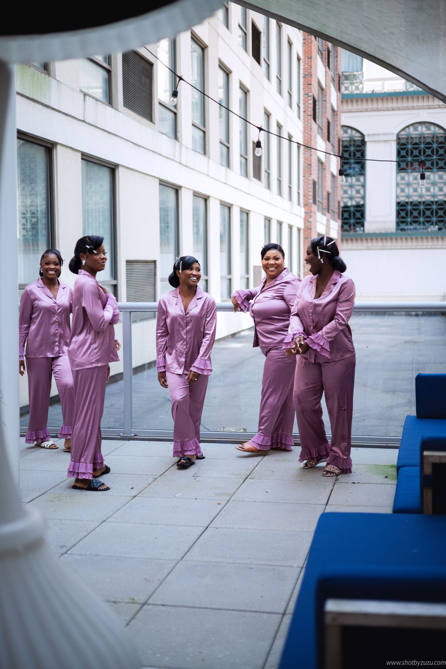 Group wearing matching pink silk pajamas gathered in outdoor courtyard.