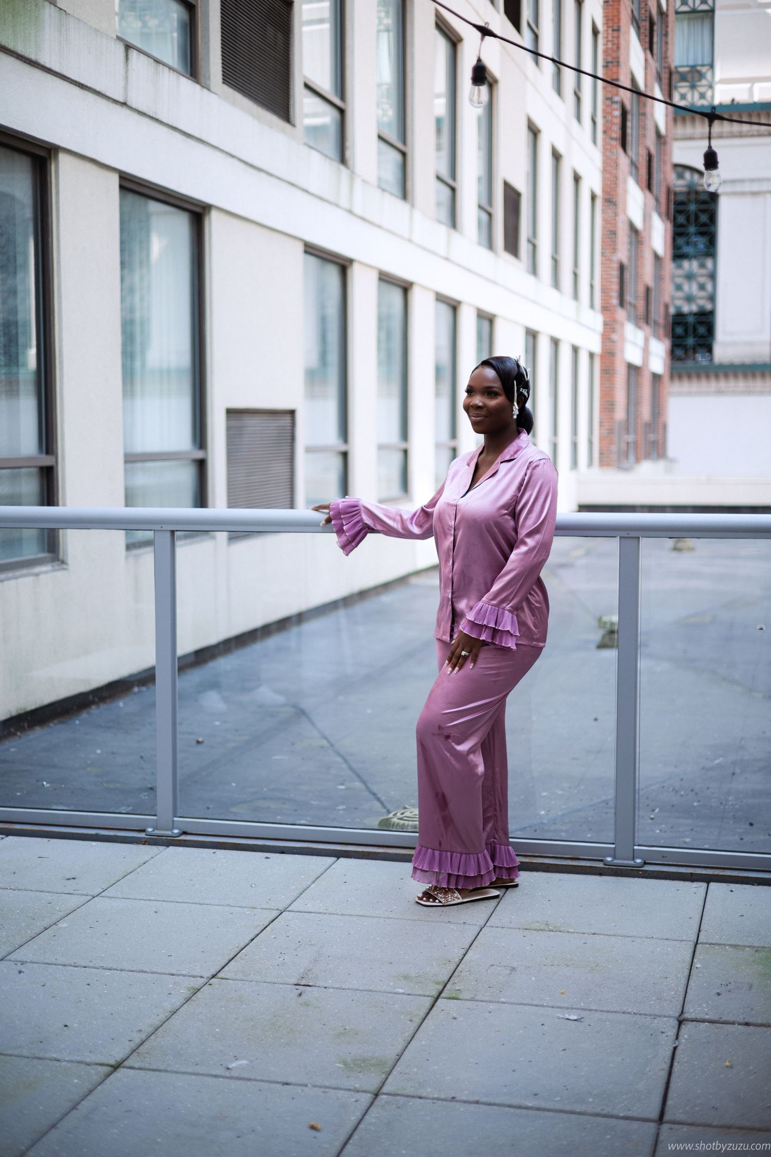 Woman in pink ruffled pajama set stands on outdoor terrace.