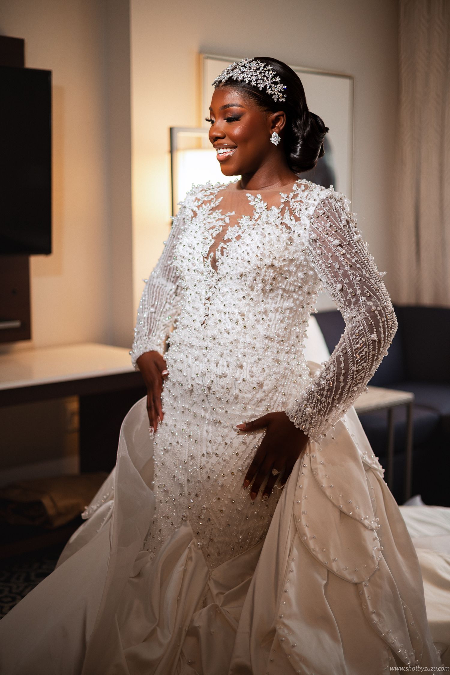 A joyful bride poses in a beaded long-sleeve wedding gown with crystal accessories.