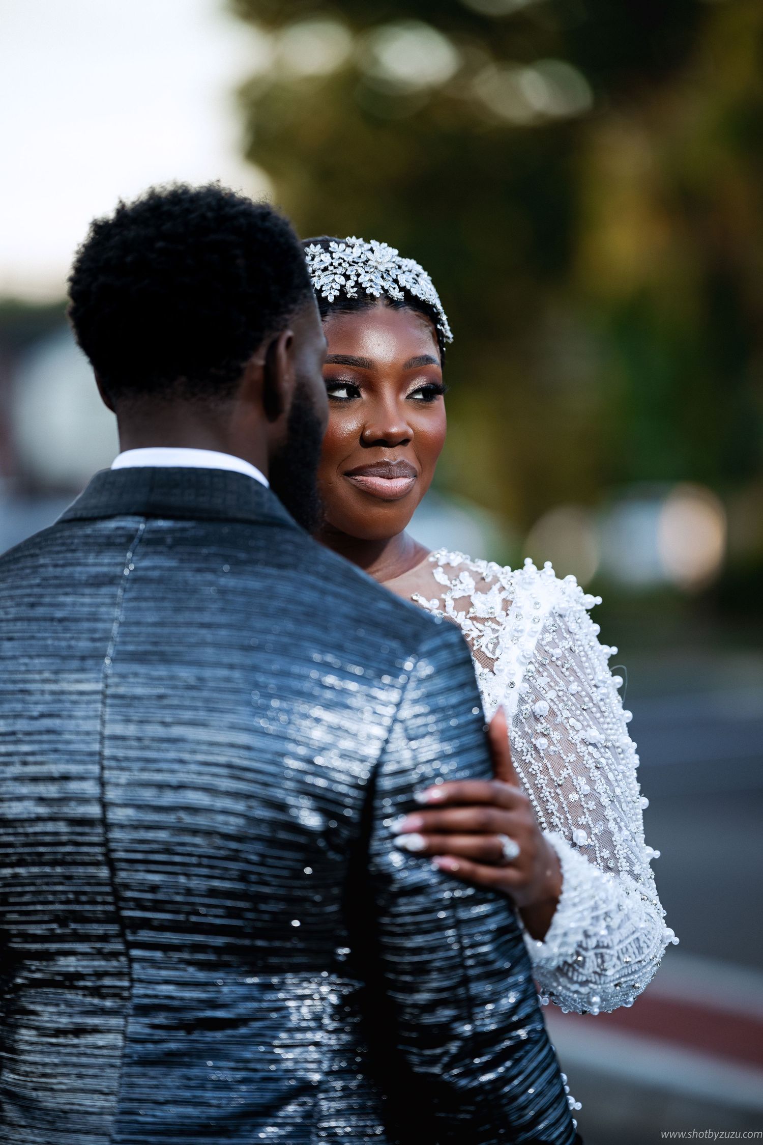 A tender outdoor wedding portrait showing the bride in a crystal tiara and beaded gown with her groom.
