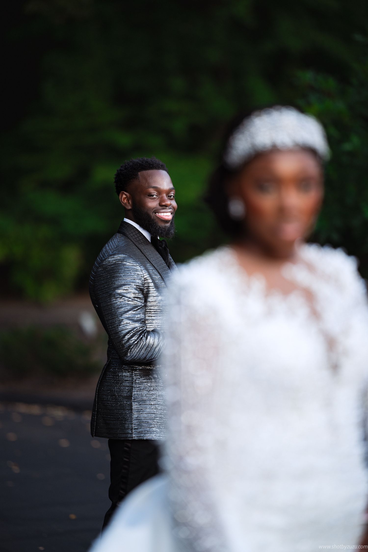Wedding portrait with metallic gray suit in foreground and white dress in soft focus background.