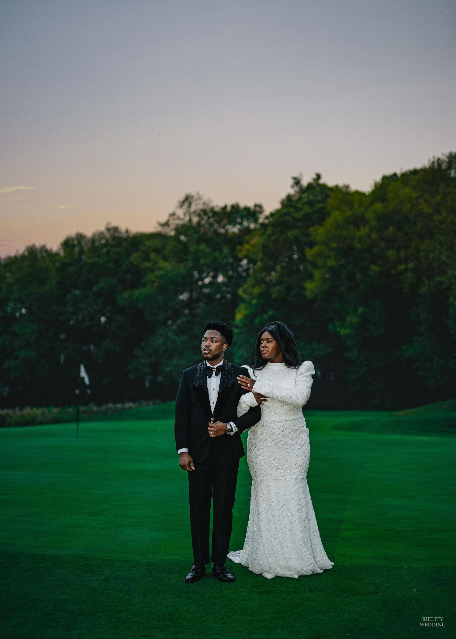 A couple takes romantic wedding photos at sunset on a lush green golf course.