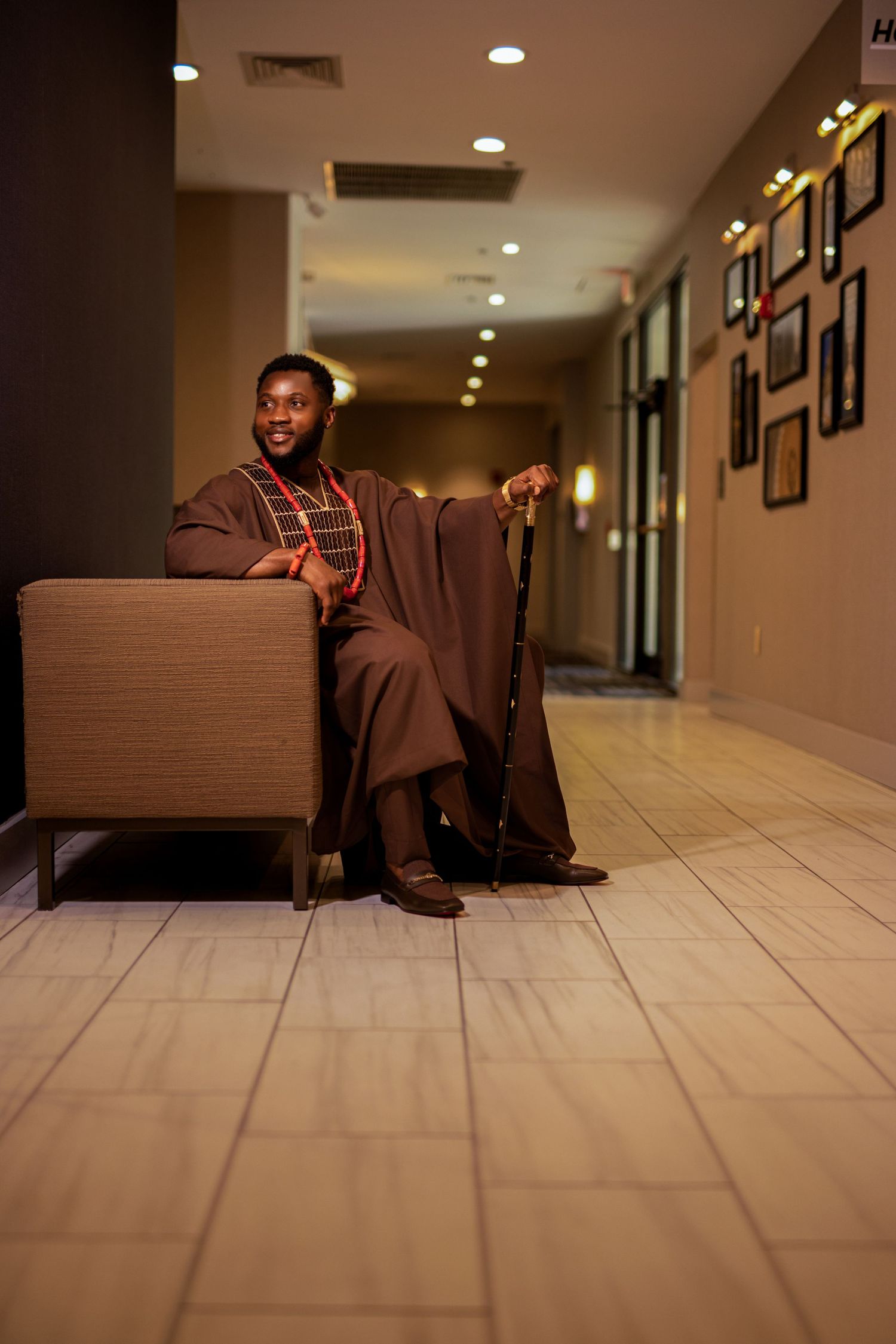 Low angle shot of person in brown outfit seated on couch in hotel hallway.