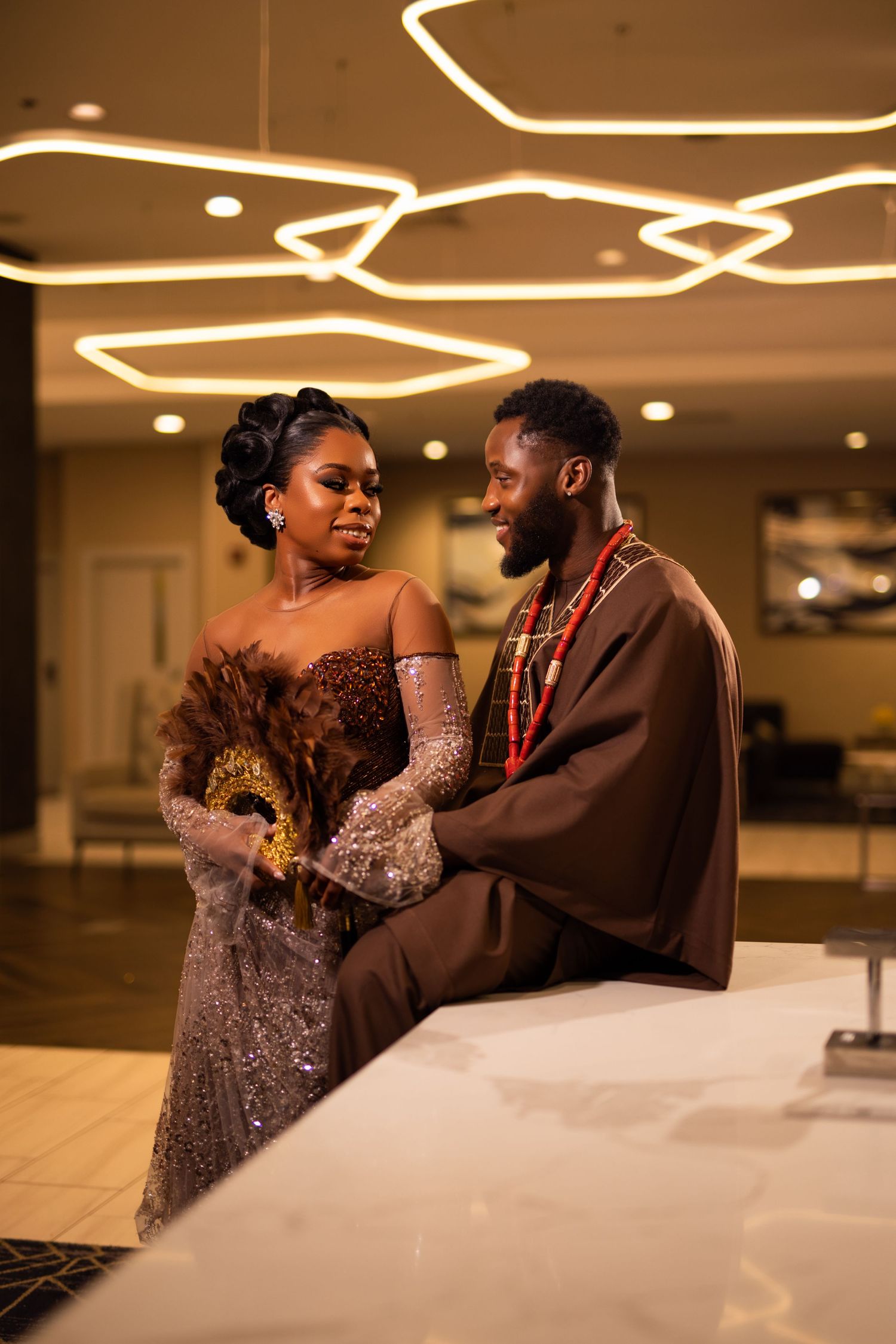 Couple shares an intimate moment at an elegant venue with decorative lighting and formal attire.