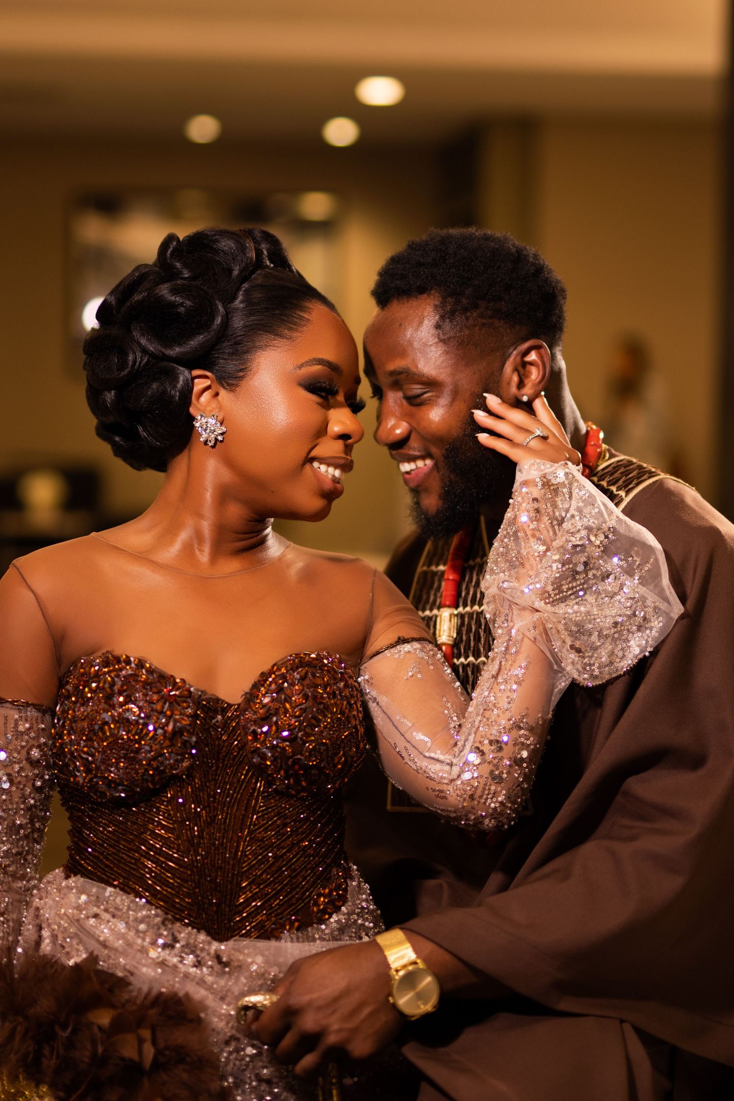 Couple in formal attire shares a tender moment under warm lighting at an event.