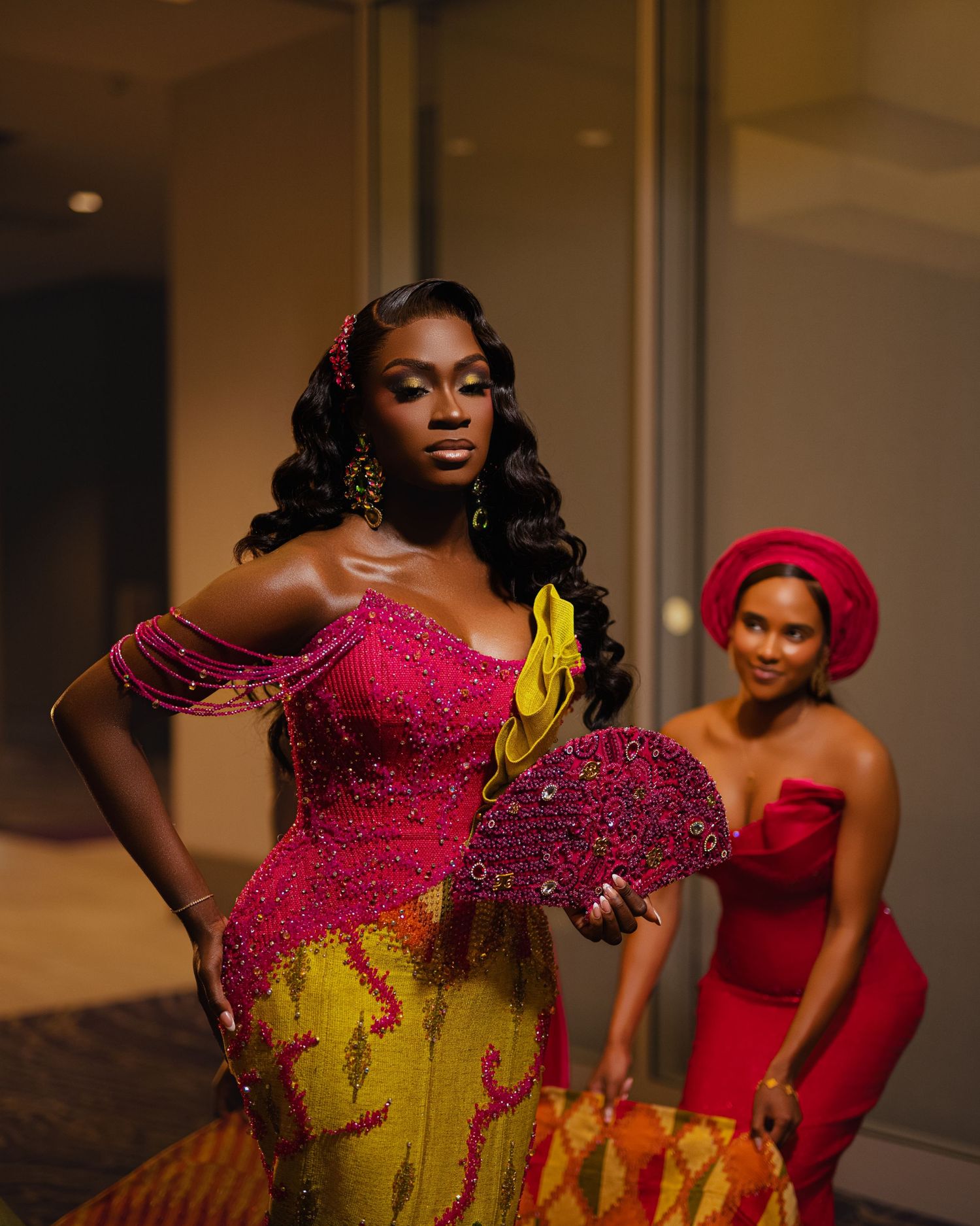 Two women in glamorous formal attire pose confidently, wearing stunning red and yellow dresses with intricate beading.