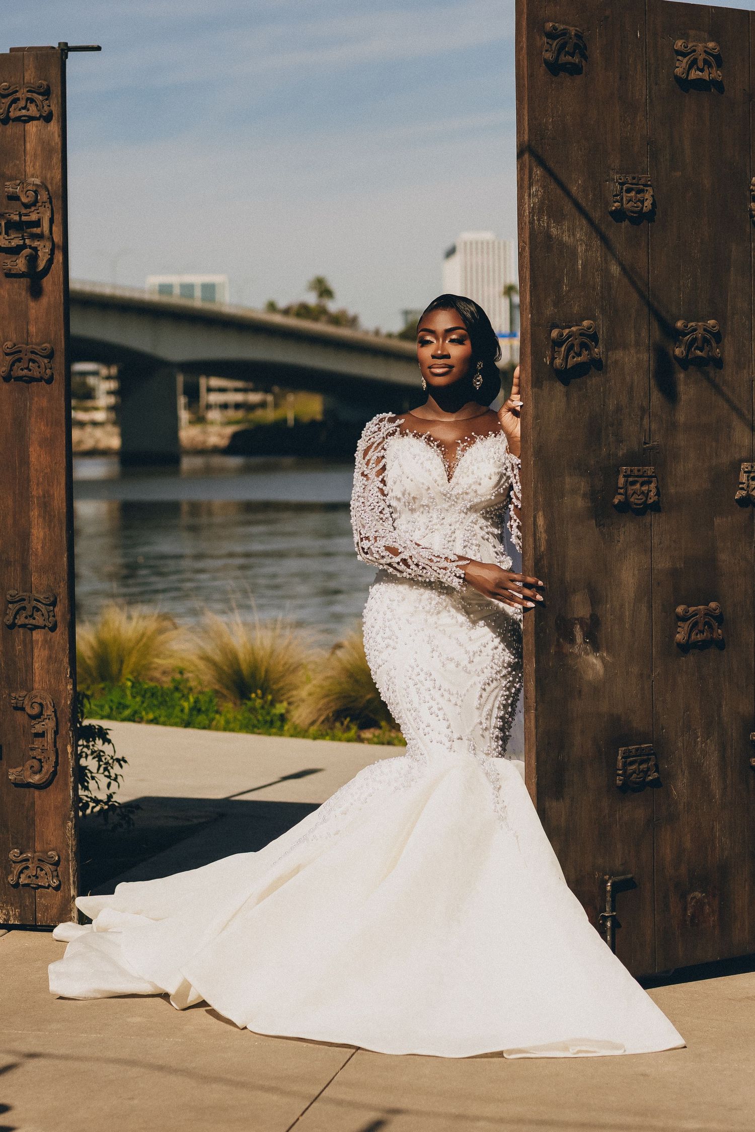 A stunning white lace mermaid wedding dress photographed against rustic metal doors near a waterfront.