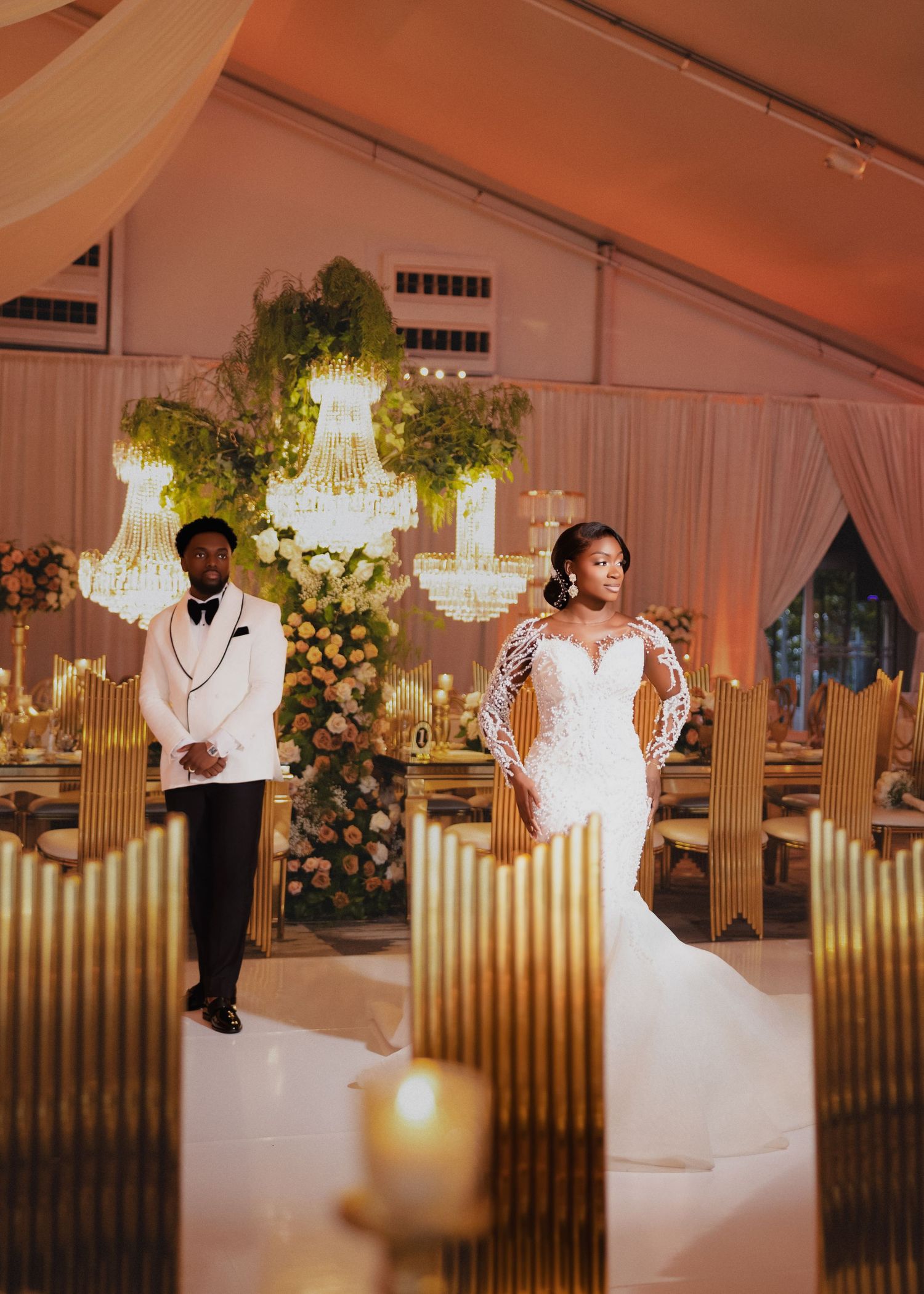 Luxurious wedding reception setup with gold decor, chandeliers, and floral arrangements in an elegant tent venue.