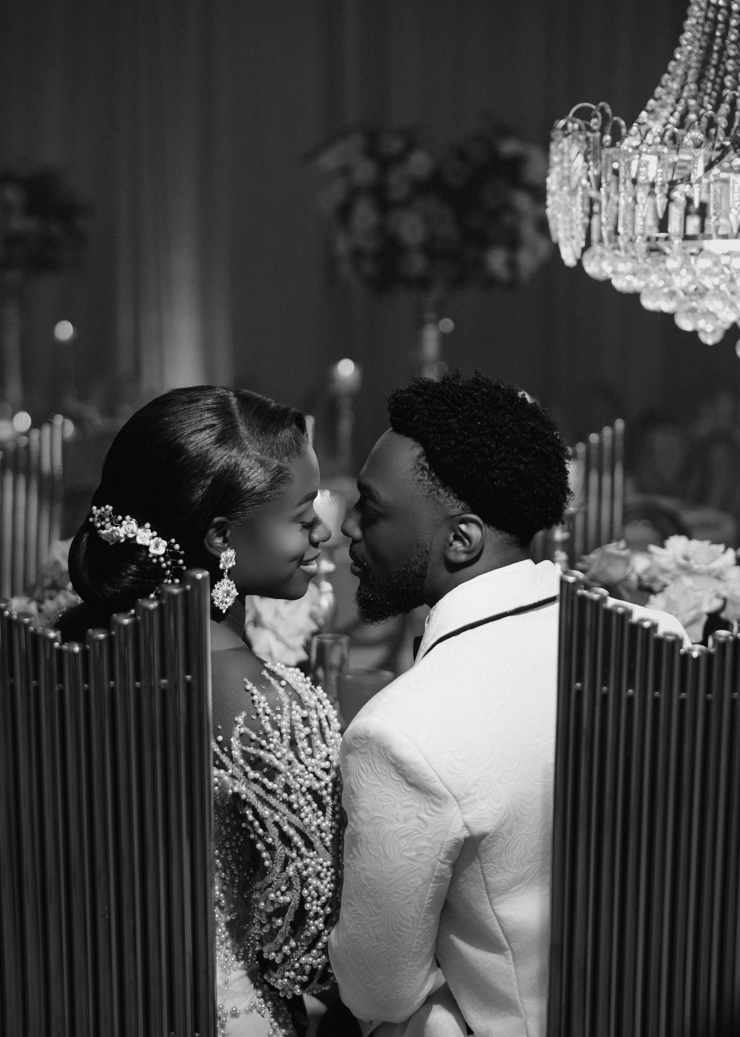 An intimate black and white portrait of a couple sharing a romantic moment beneath a crystal chandelier.