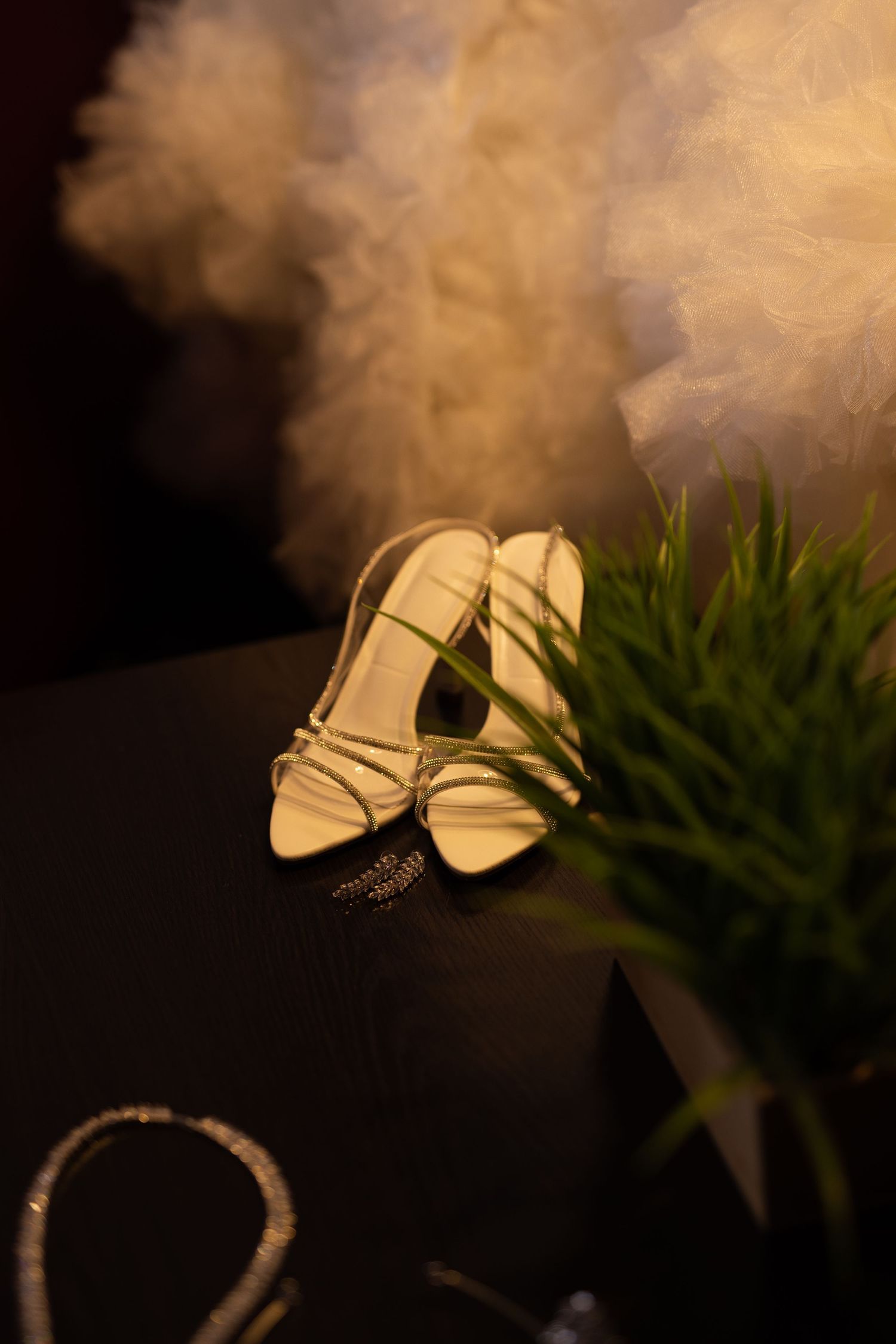 Elegant white strappy wedding heels displayed against dark background with soft lighting.