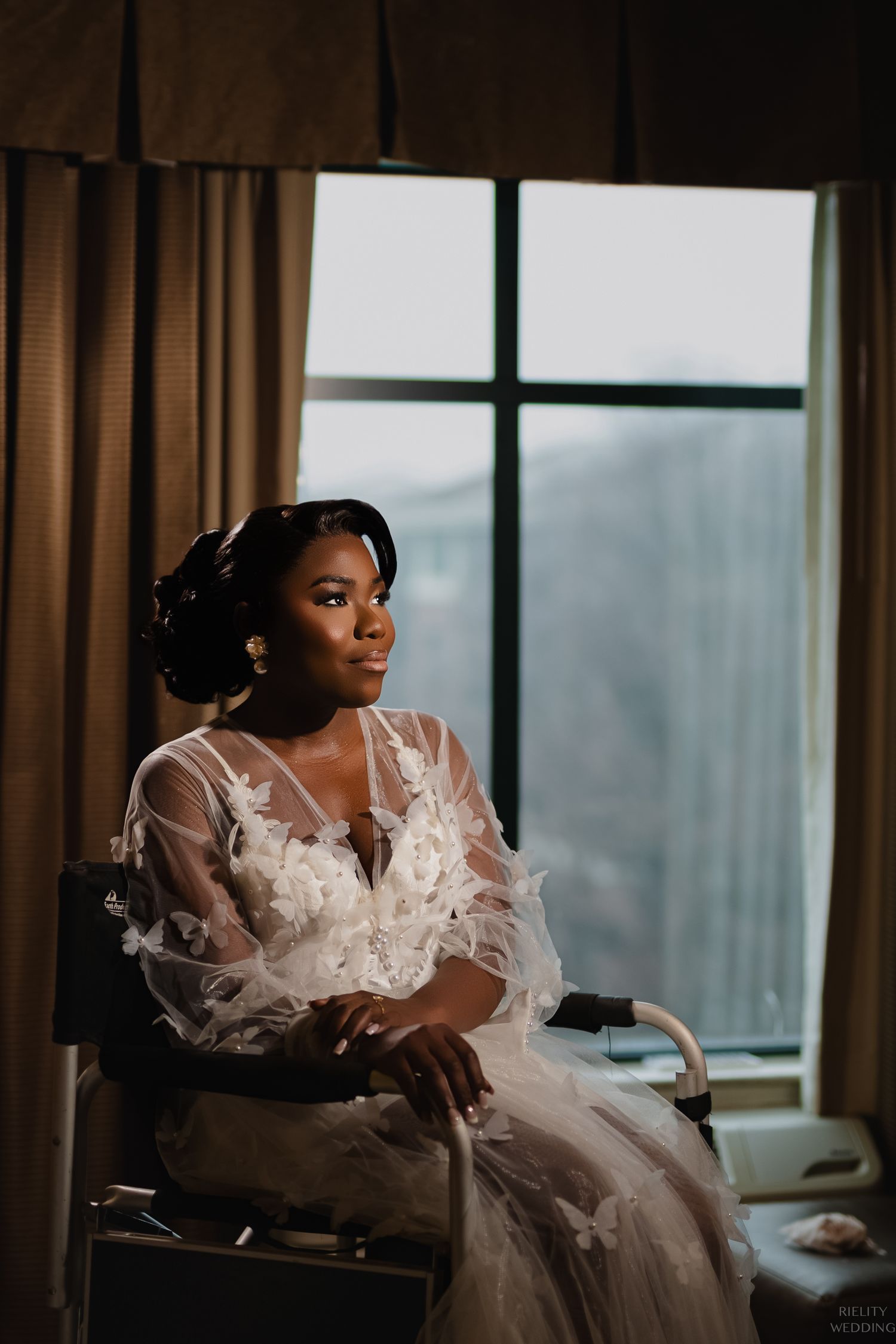 Romantic bridal portrait by window in flowing sheer gown with butterfly details.