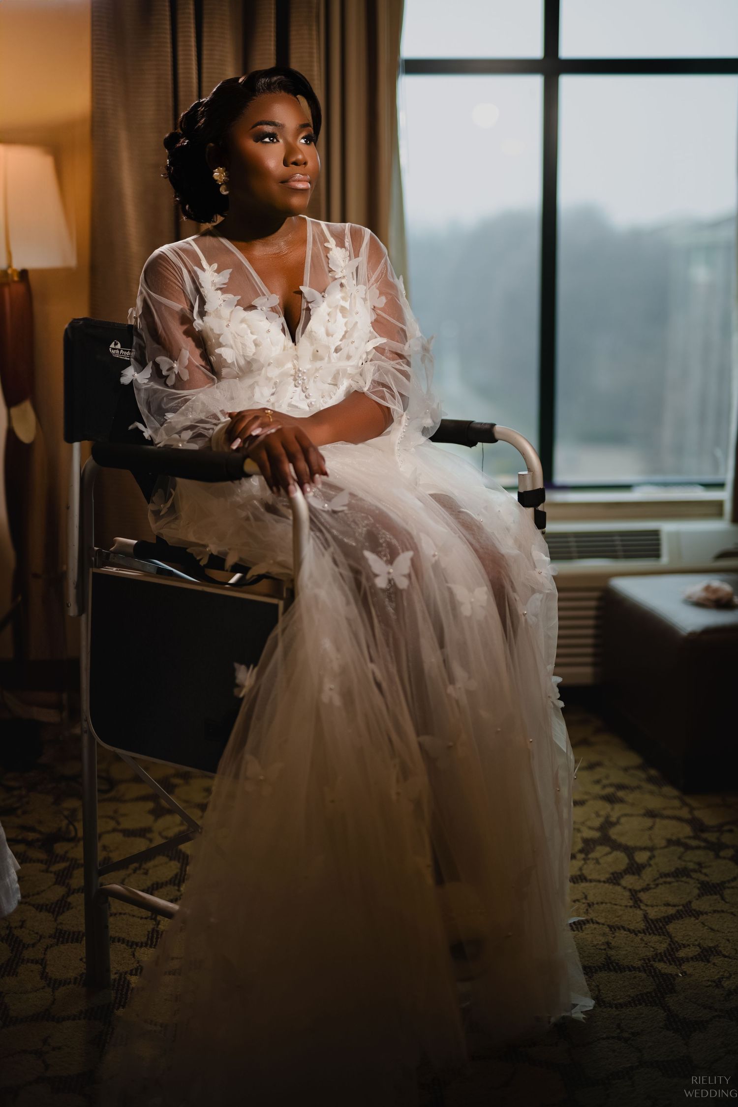 Moody bridal portrait in front of window wearing ethereal sheer gown.
