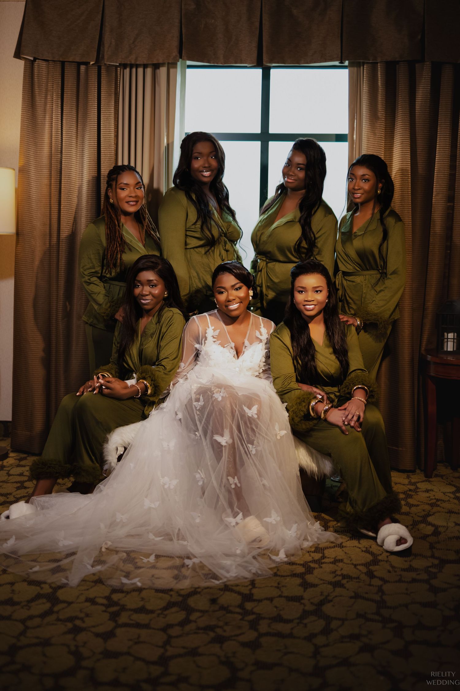 Bridal party poses together with bridesmaids in olive green dresses surrounding bride in white gown.