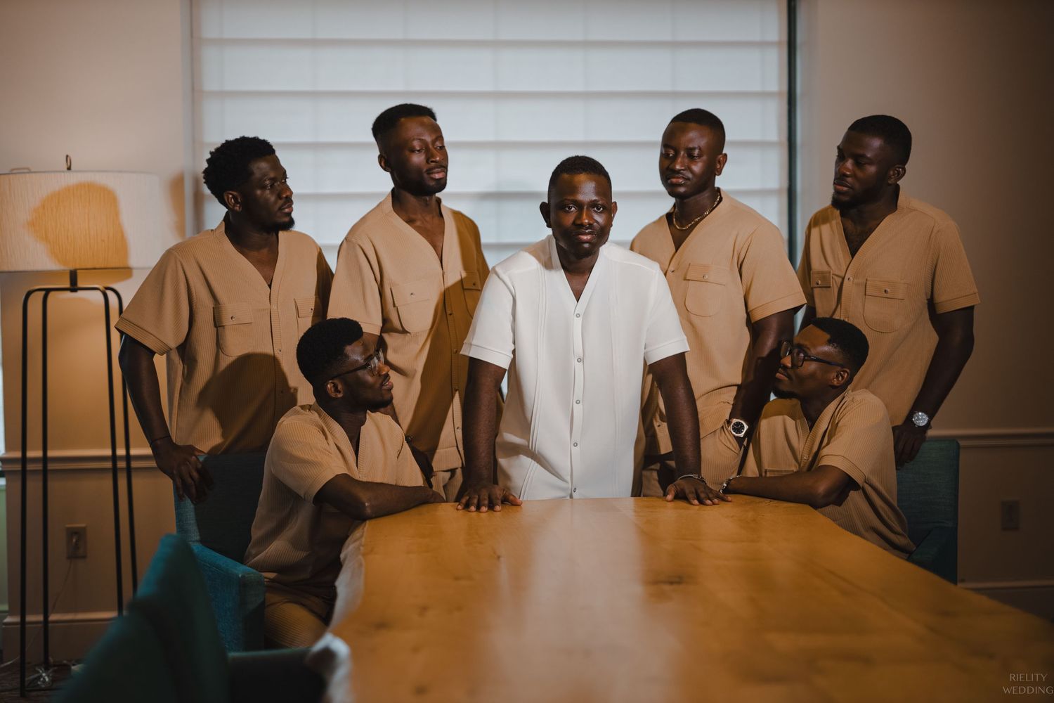 Group of men in formal attire gather around wooden table for professional photo.
