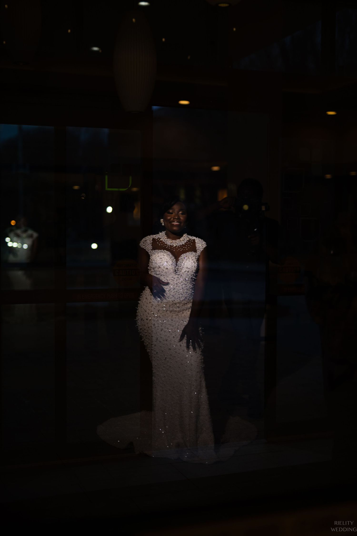 Silhouette of person in beaded wedding gown against dark background.