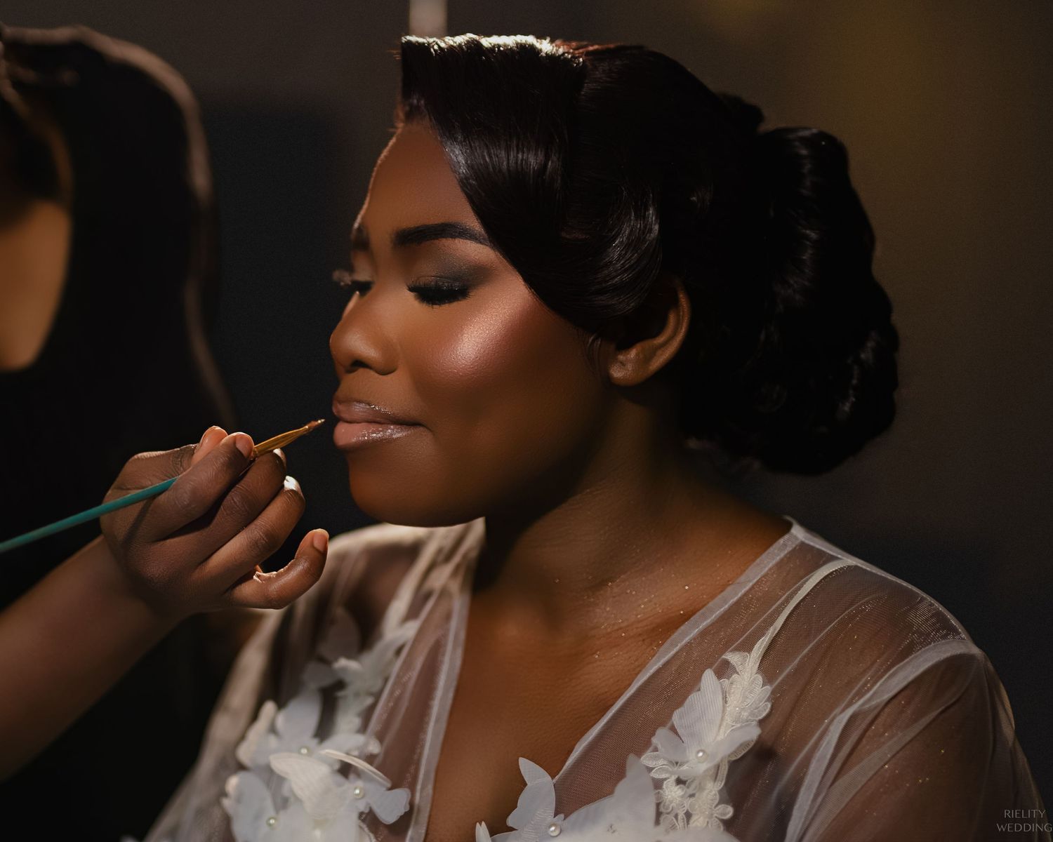 Getting ready photo showing detailed makeup application in golden light.