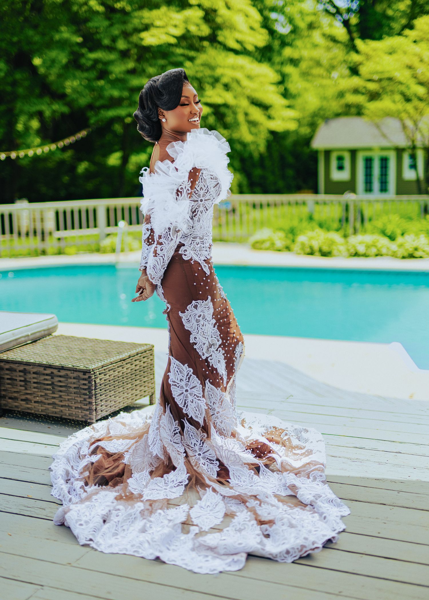 A stunning white lace wedding dress with sheer details and a dramatic train photographed by a poolside.