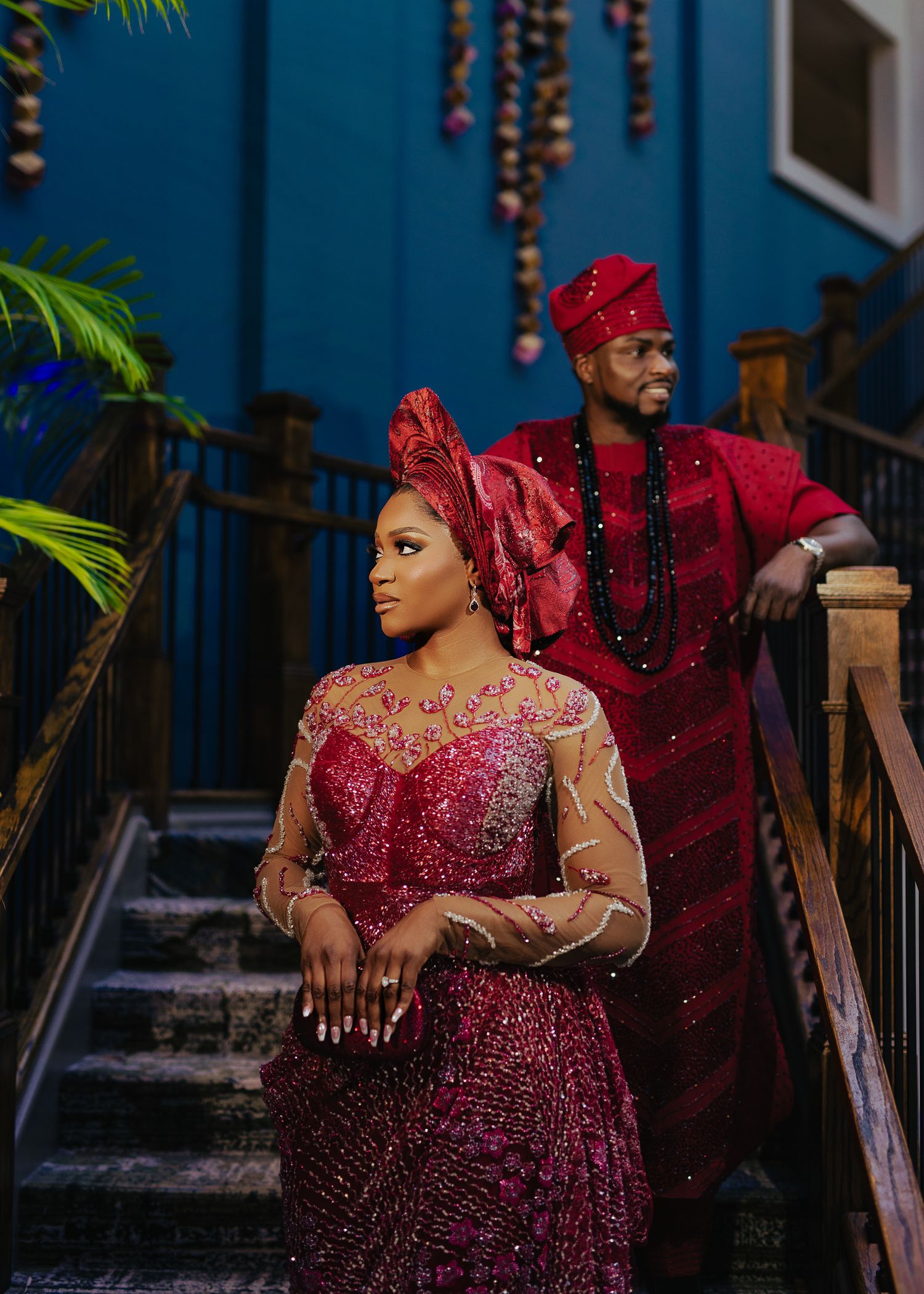 Person wearing a sparkling burgundy gown poses on stairs with blue wall backdrop.