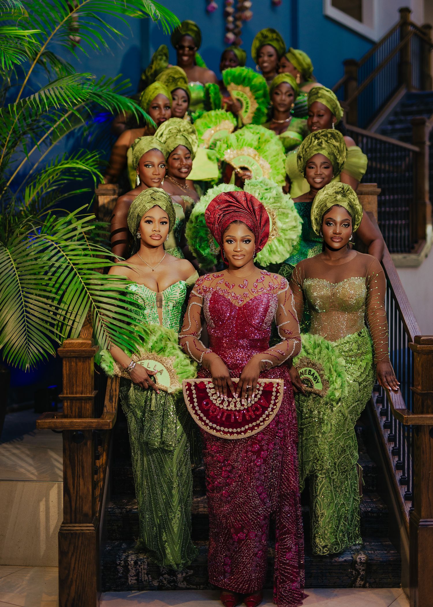 Wedding party members pose in elegant green and burgundy traditional Nigerian attire with dramatic feather details.