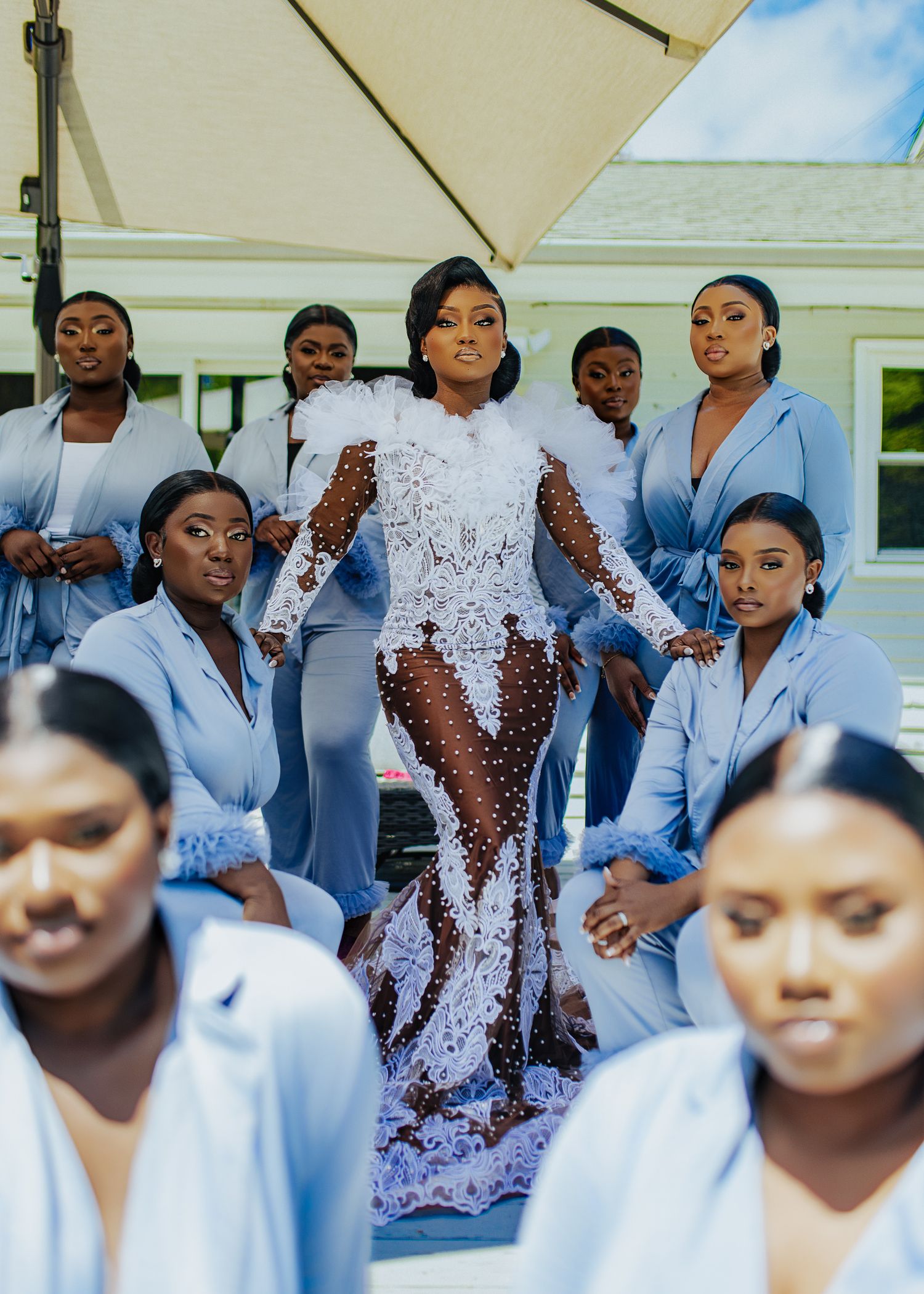 A group of people in light blue dresses stand together for a formal photo shoot outdoors.