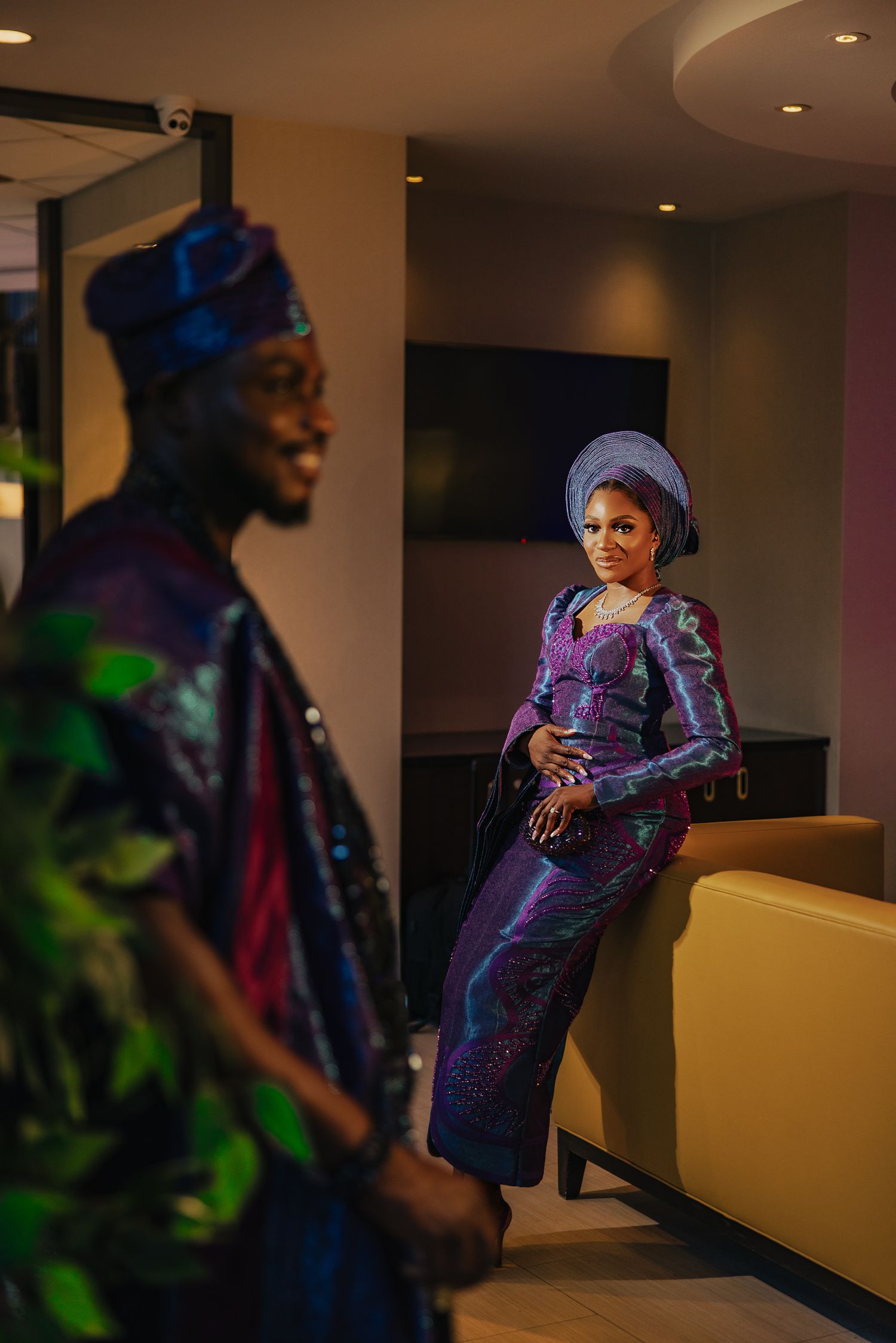 Person in a shimmering purple dress poses elegantly in an indoor setting with mood lighting.