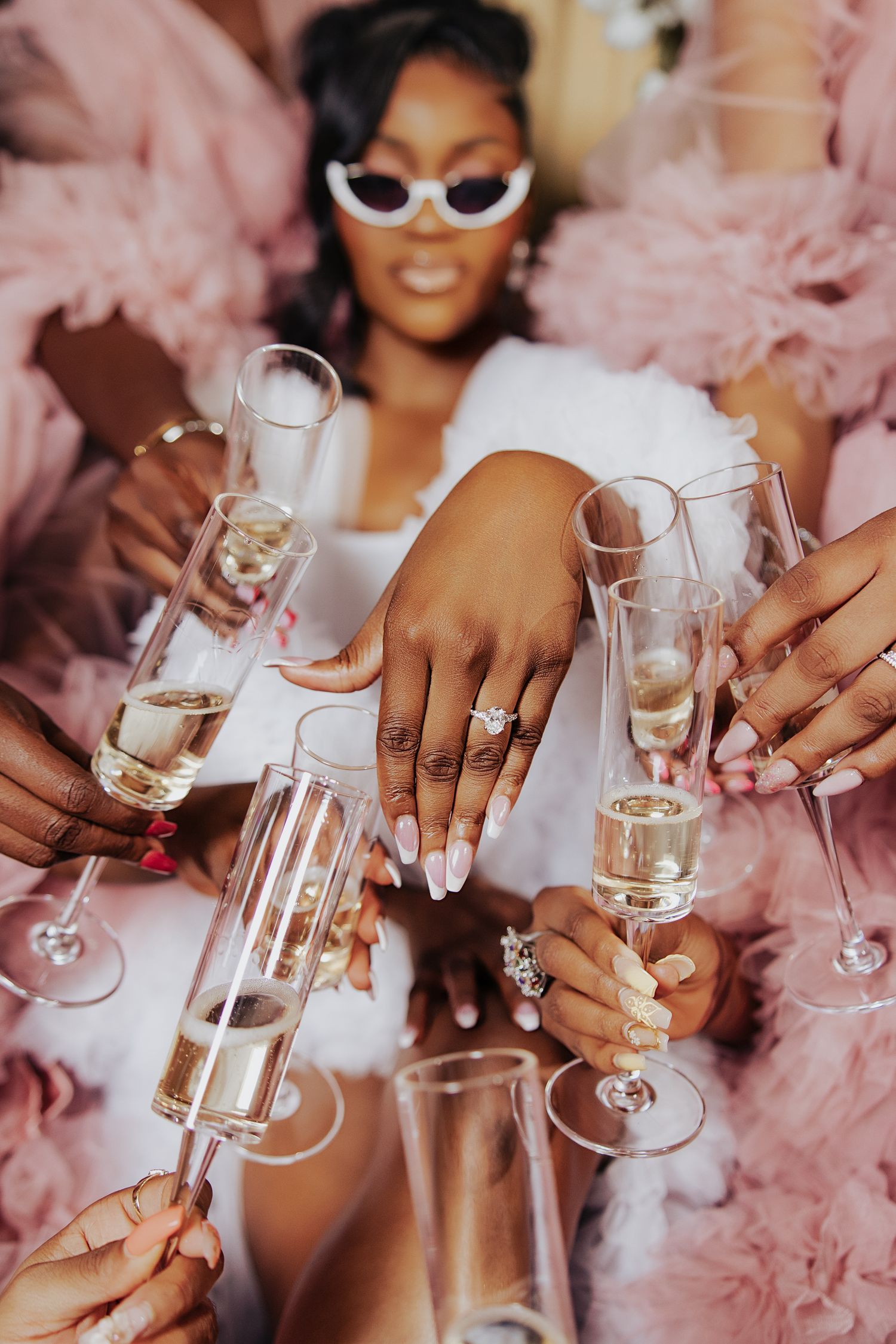 Champagne glasses clink together amidst pink tulle fabric and sparkling jewelry.