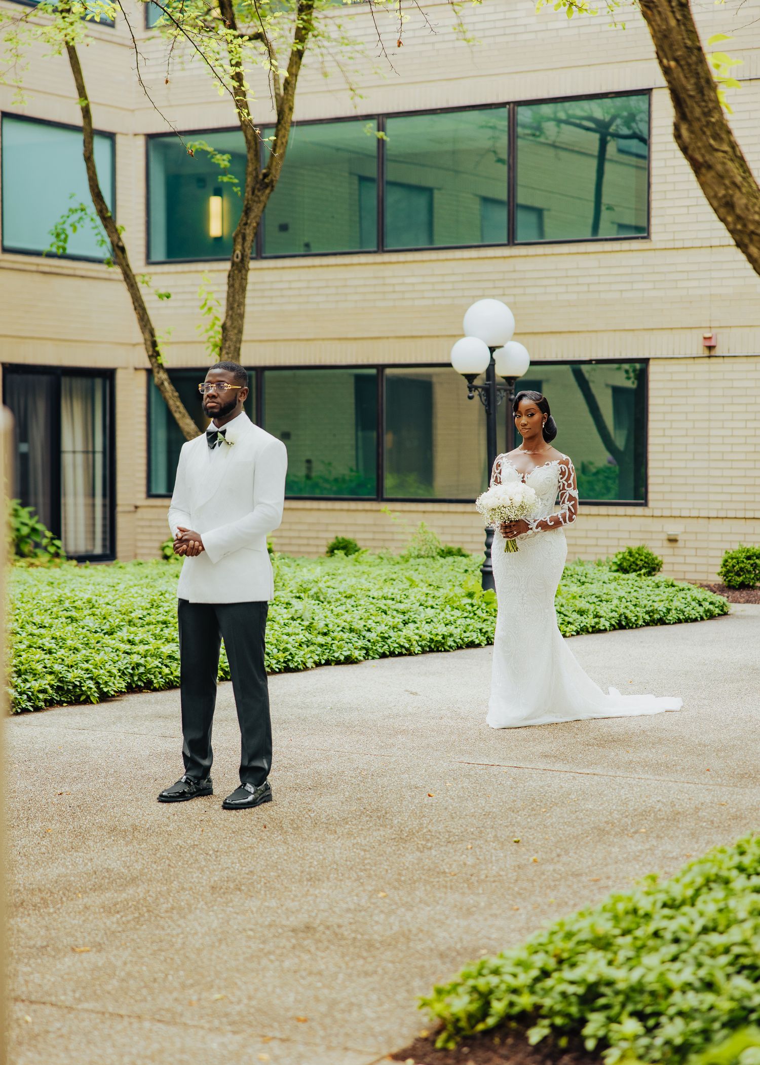 Wedding party members walk outside a modern building with white brick walls and glass windows.