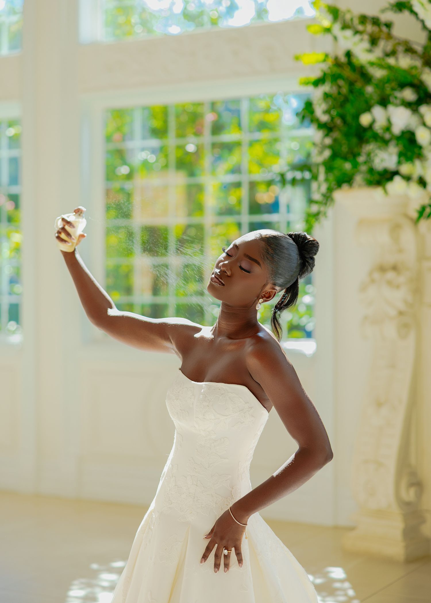 Joyful figure in a white strapless wedding gown dances in a sunlit room with large windows.