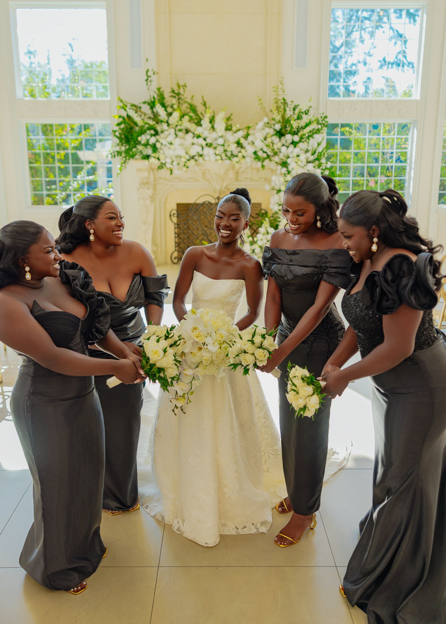 Bridesmaids in charcoal gray dresses pose playfully in a bright indoor venue.