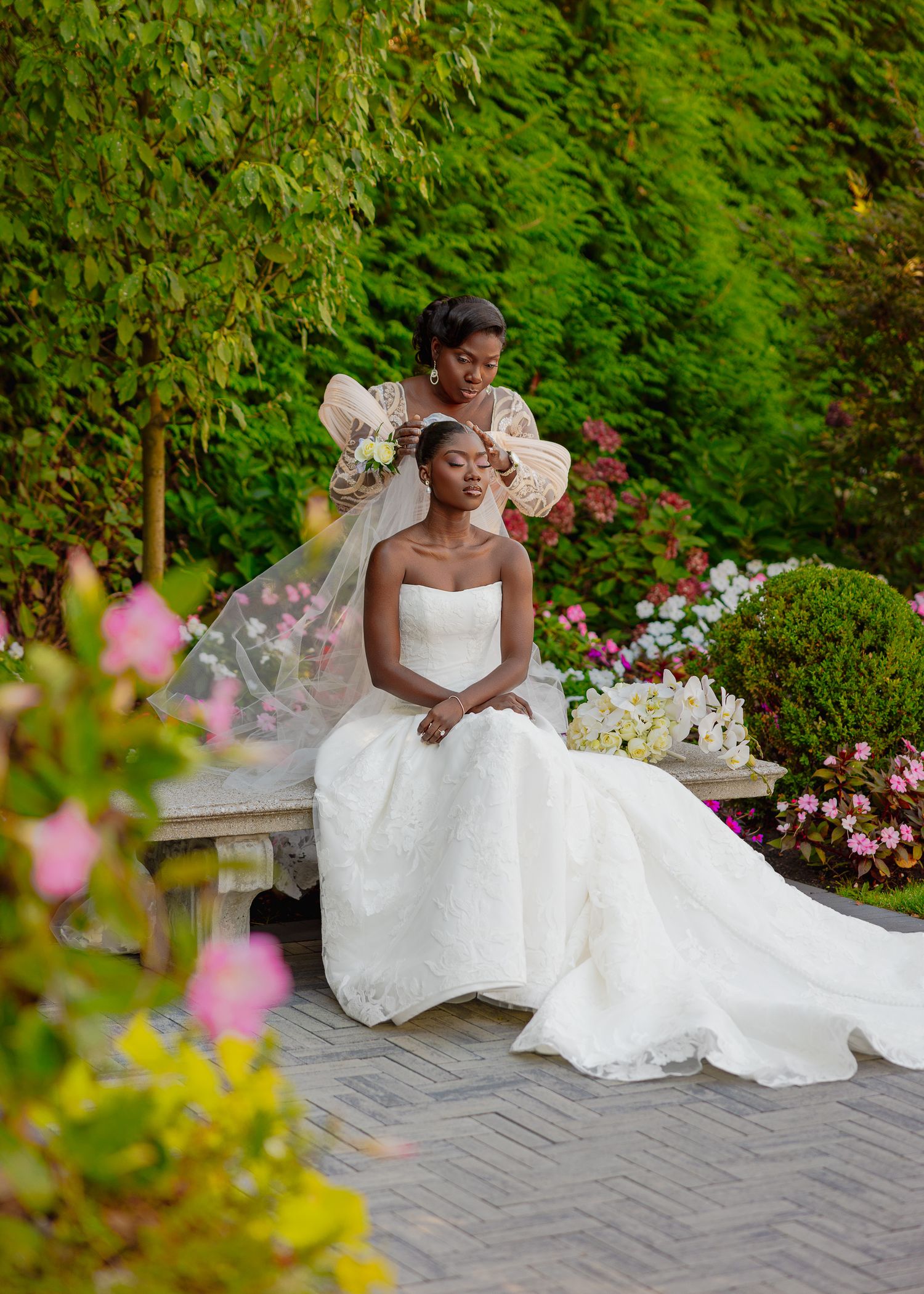 Bride in white wedding gown poses gracefully on stone bench in garden setting.
