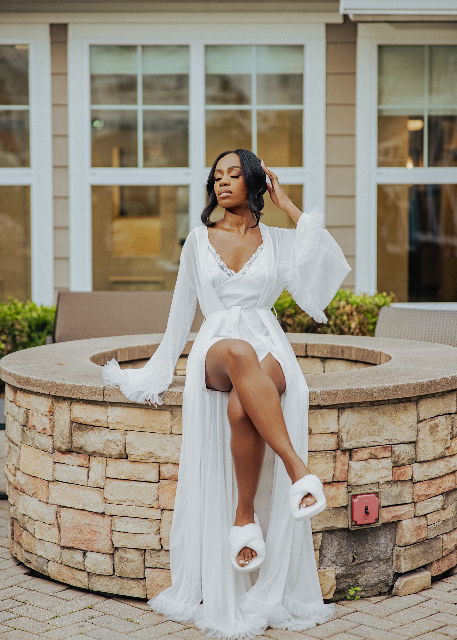 Woman in white dress poses gracefully on stone wall outdoors with flowing fabric creating elegant movement.