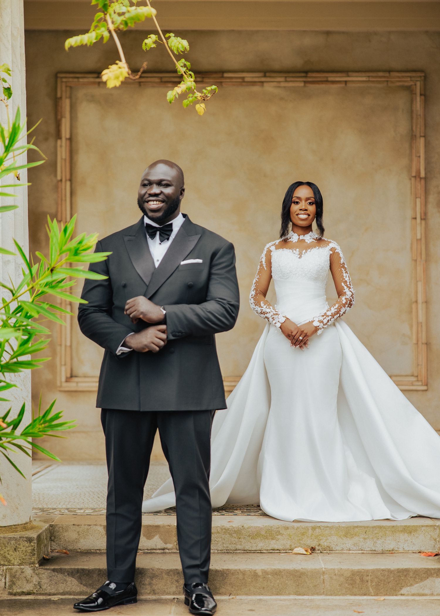 A romantic wedding photo series showing a couple in formal attire posing against a rustic wall with green foliage.
