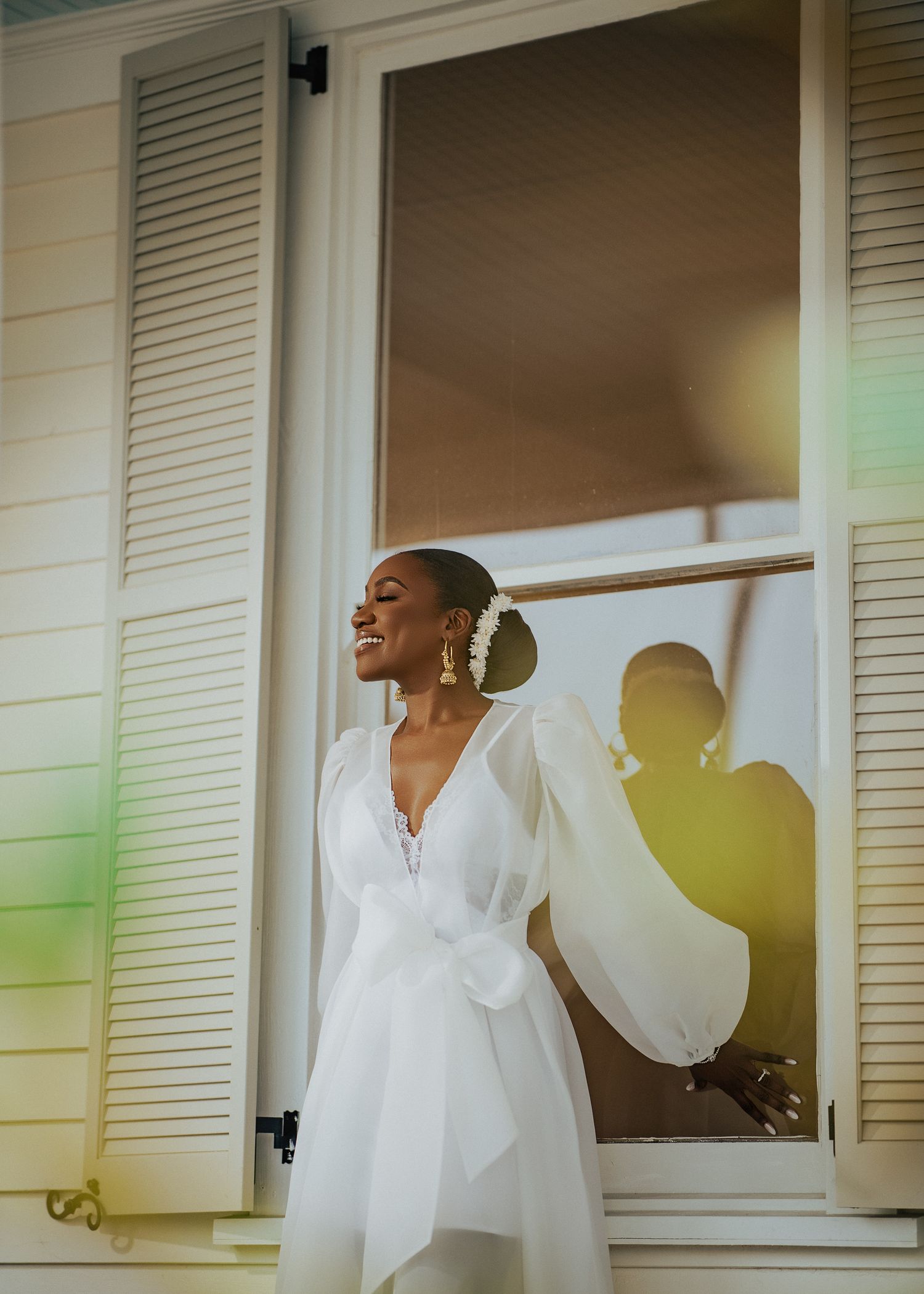 Person in white robe dances joyfully near window with natural light streaming in.