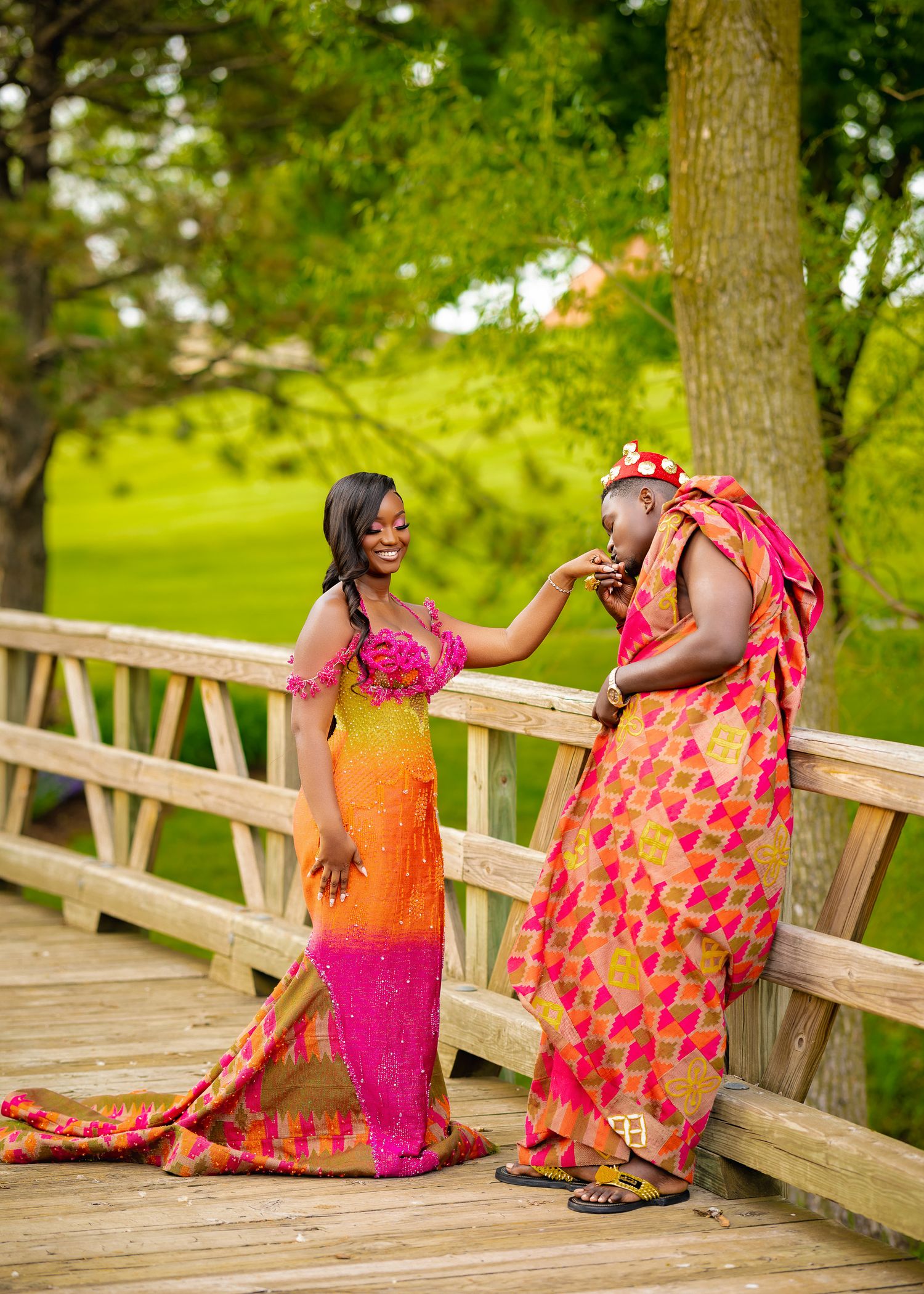 Vibrant orange and pink dresses create a colorful scene on a wooden bridge in a lush green park setting.