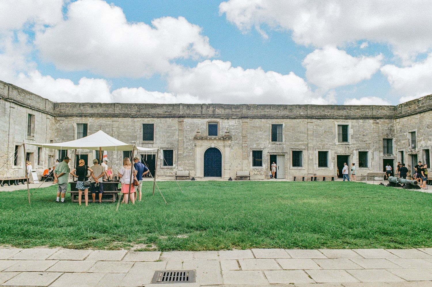 Historic stone courtyard with green lawn and visitors exploring the grounds.