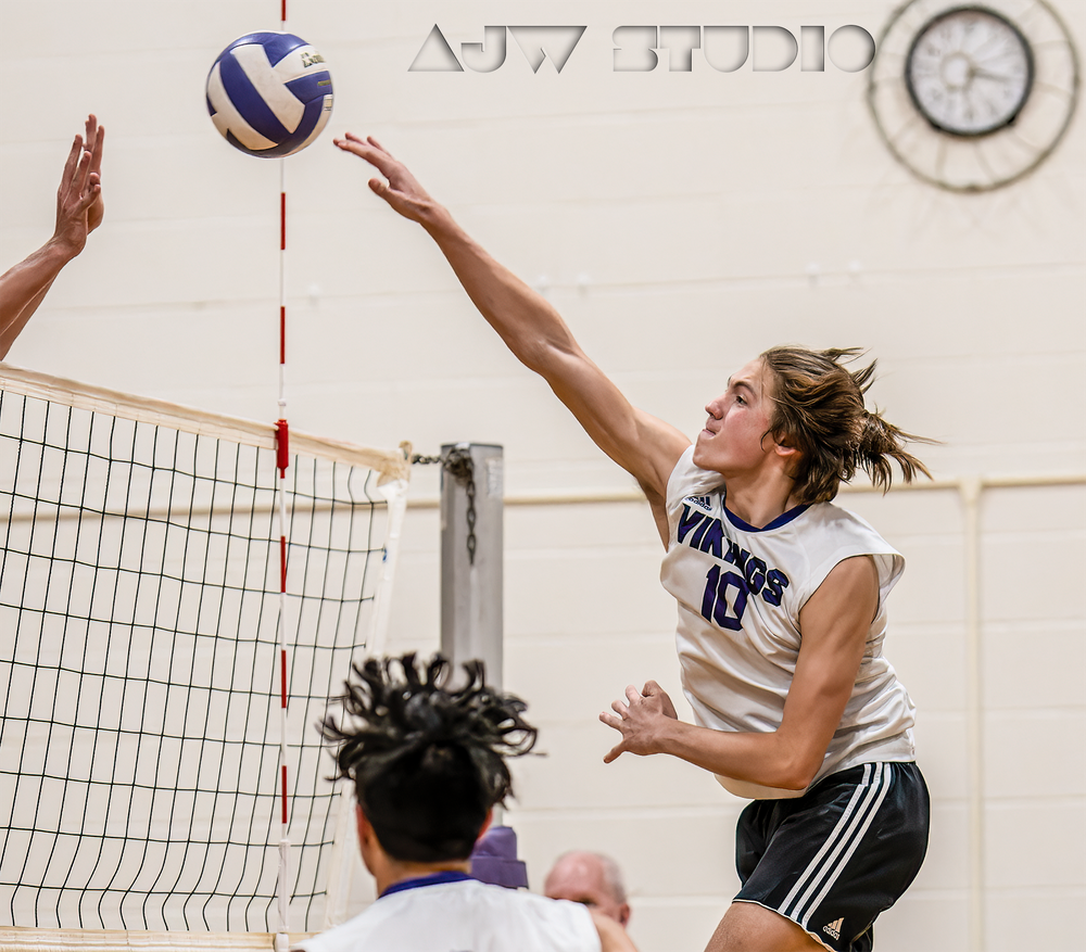 Volleyball player leaps high to spike the ball over the net during an intense indoor match.