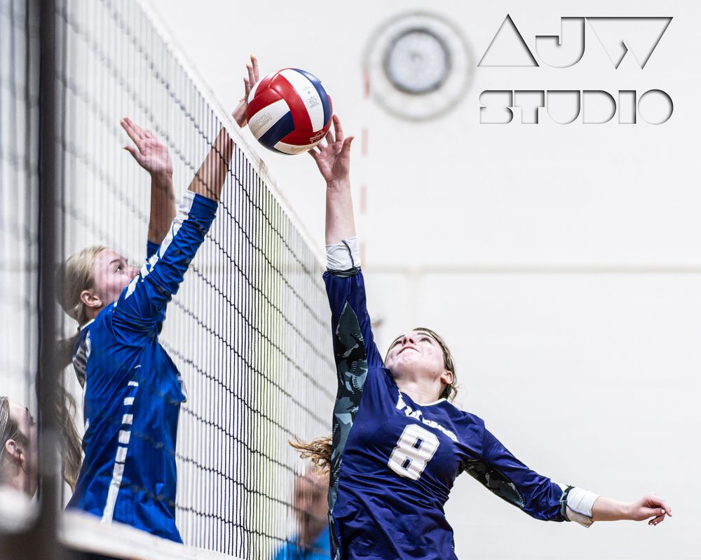 Two volleyball players jumping at the net competing for the ball during a match.