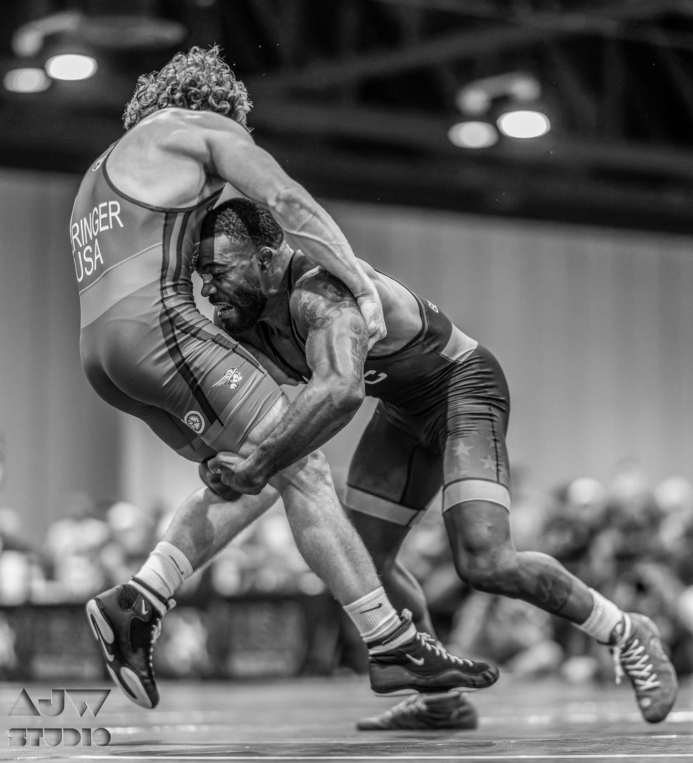 Dramatic wrestling move captured as one athlete lifts opponent during competitive match.