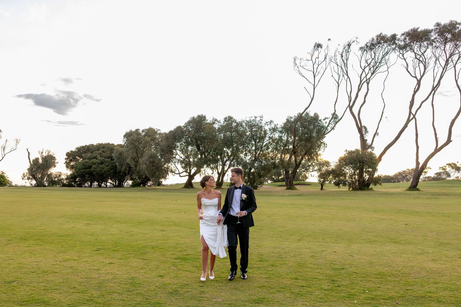 People walking together on a grassy hilltop path with cloudy skies in the background.