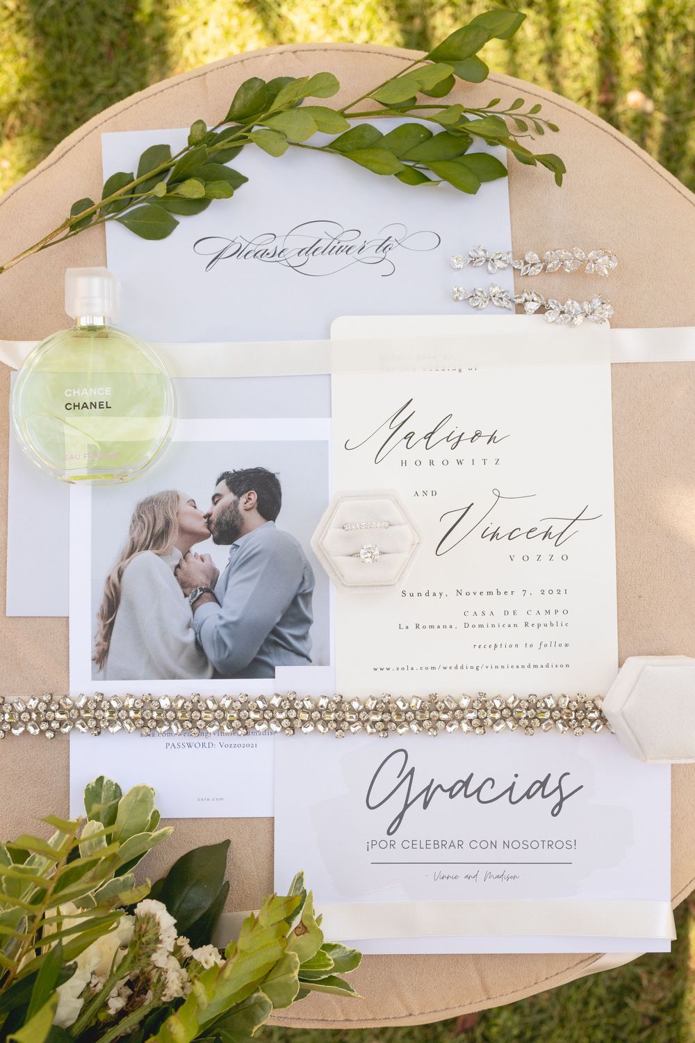 Elegant wedding invitation suite with greenery accents, Chanel perfume, and romantic engagement photo on a beige plate.