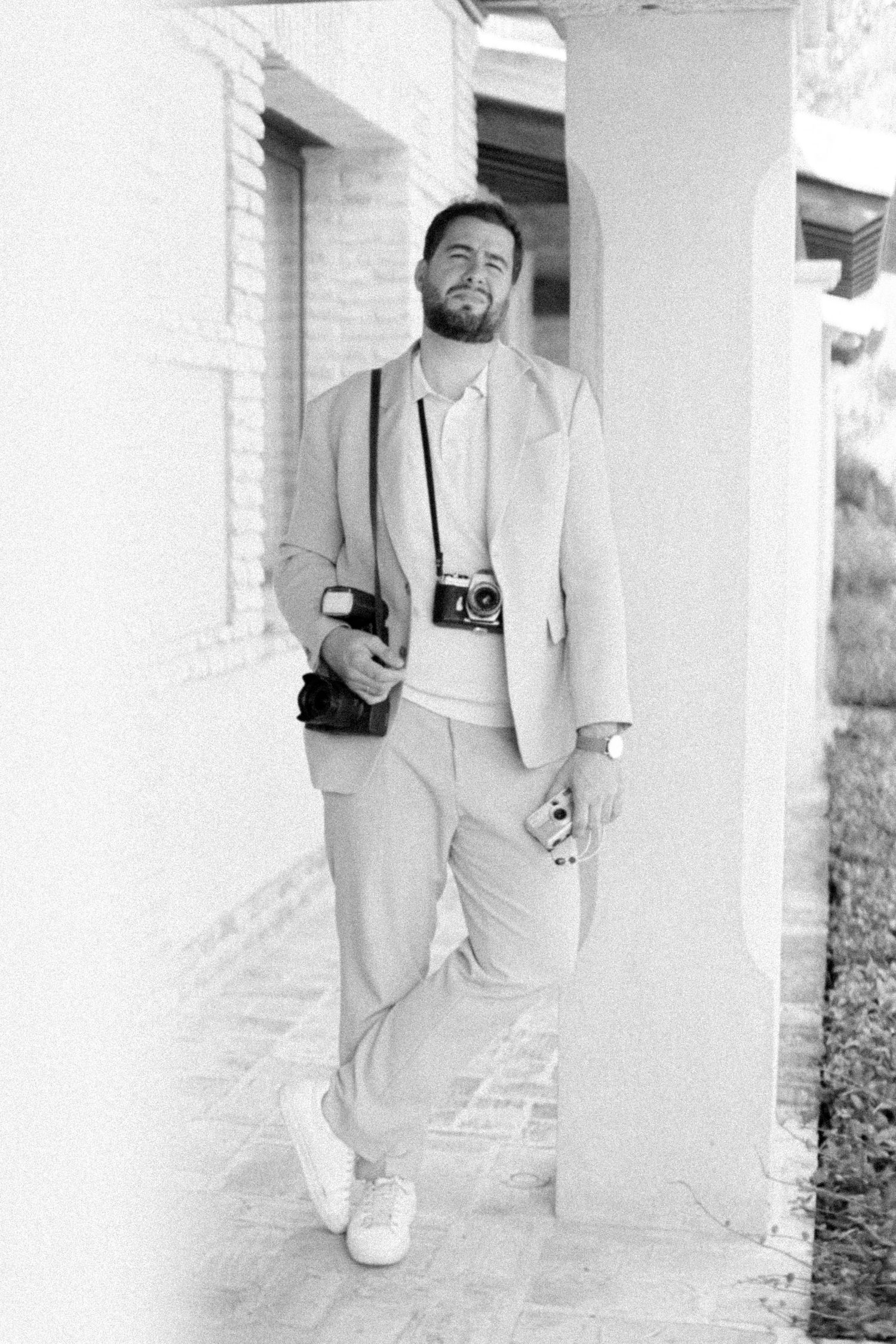 Black and white photo series showing someone walking down a covered outdoor hallway wearing a light-colored suit.