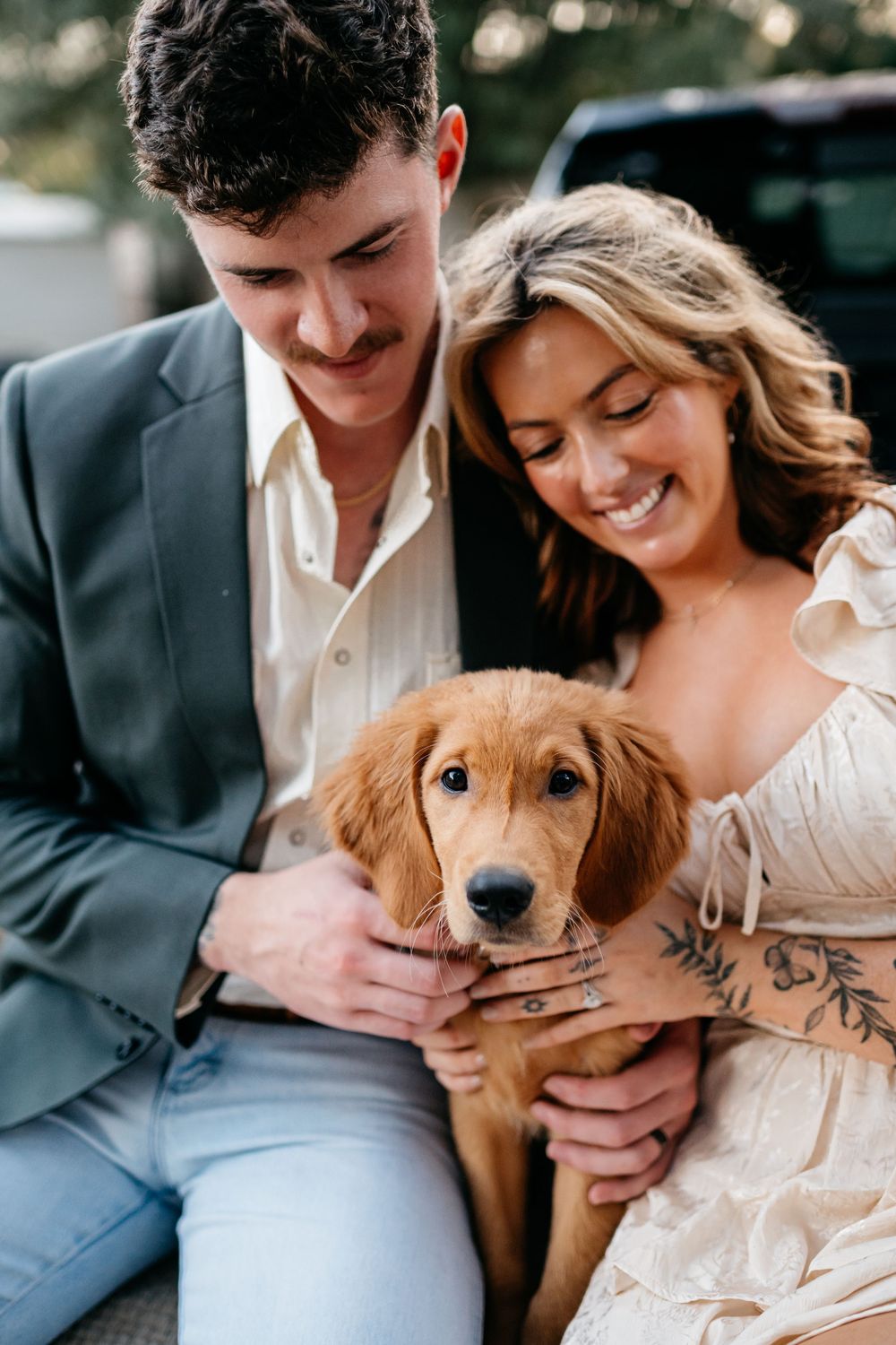 Sweet engagement photos feature a couple cuddling with their golden retriever puppy in casual attire.