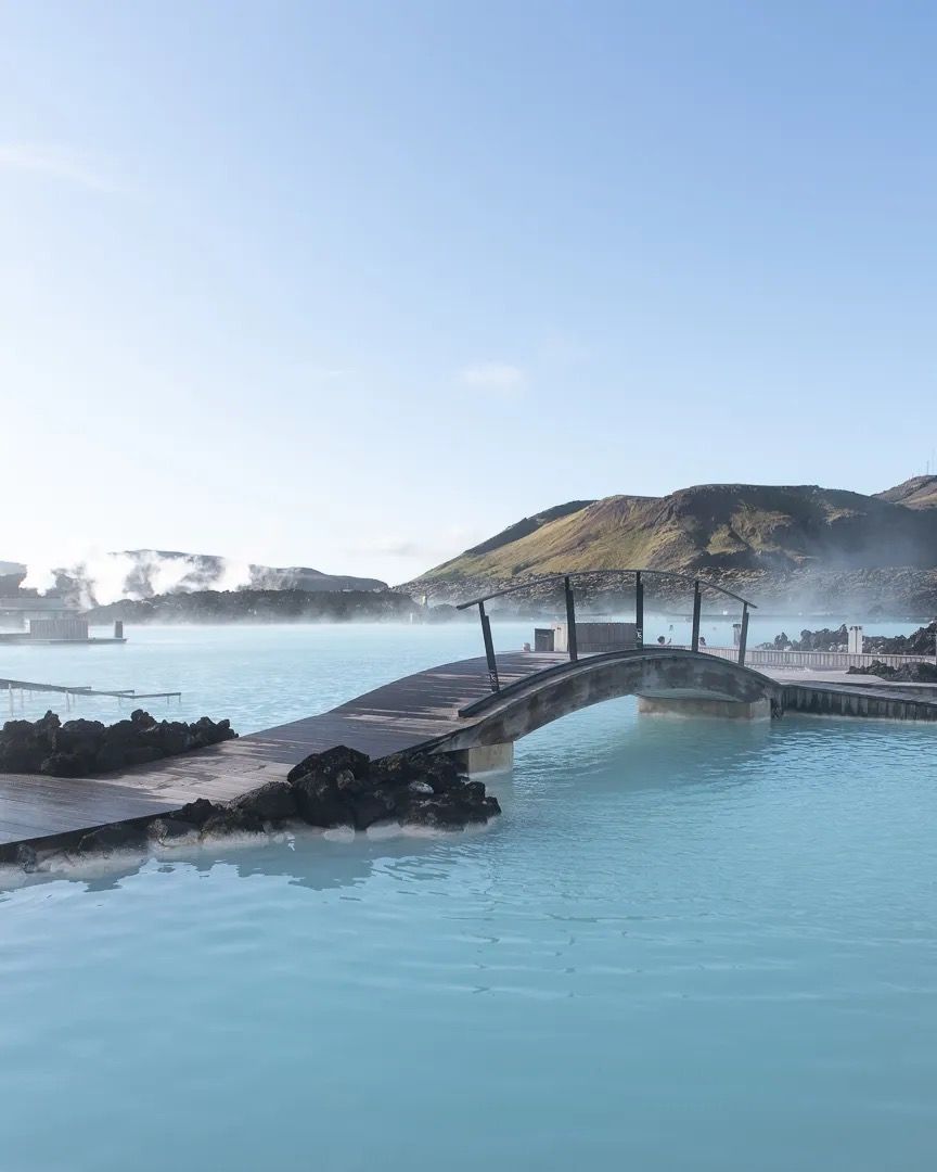 Geothermal blue lagoon with a small bridge and mountains in the background.