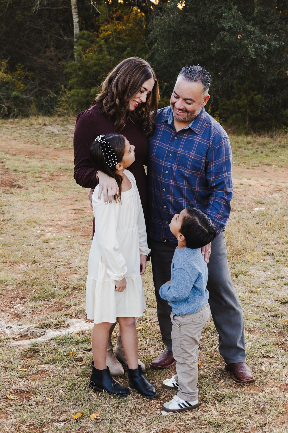 A couple playfully interacts in a casual outdoor setting with autumn foliage in the background.