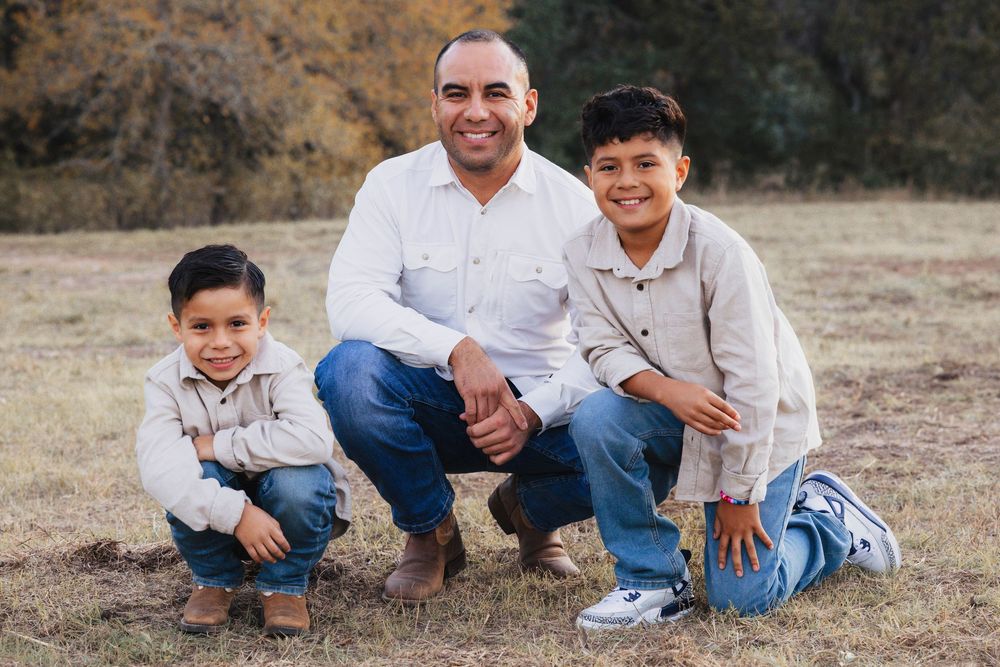 Two people sit together on brown grass in casual clothing during an outdoor photo session.
