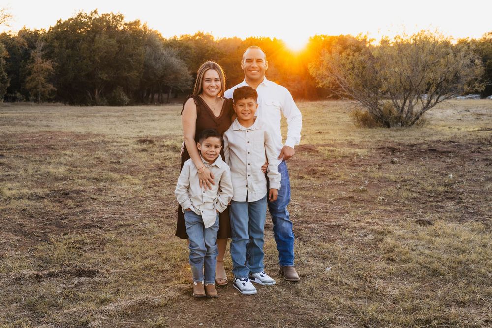 Family poses together in casual attire at sunset in a golden field with warm autumn lighting.